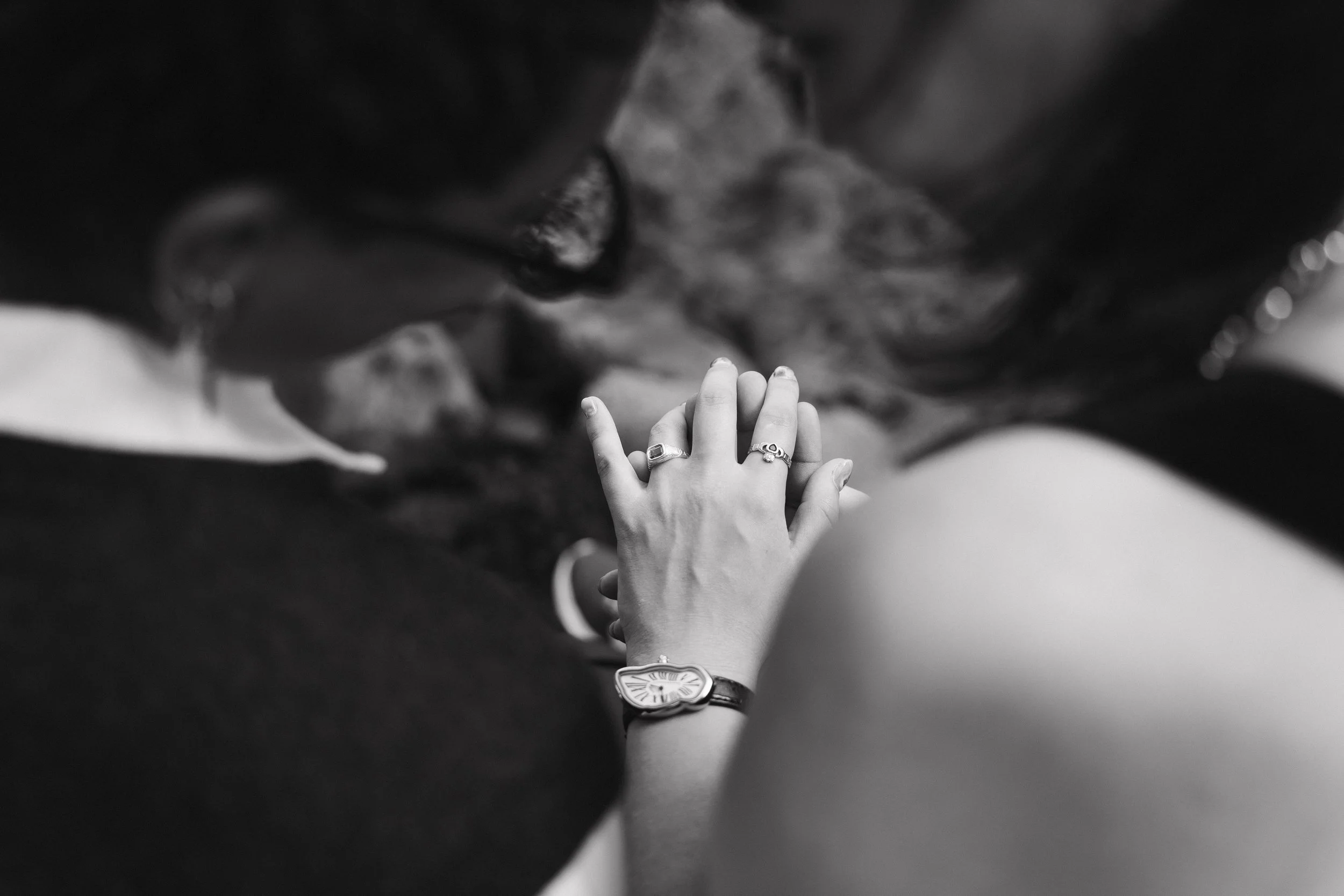 Close-up of two people holding hands, with one person wearing rings and a watch, shot in black and white. - captured by an Edinburgh wedding photographer
