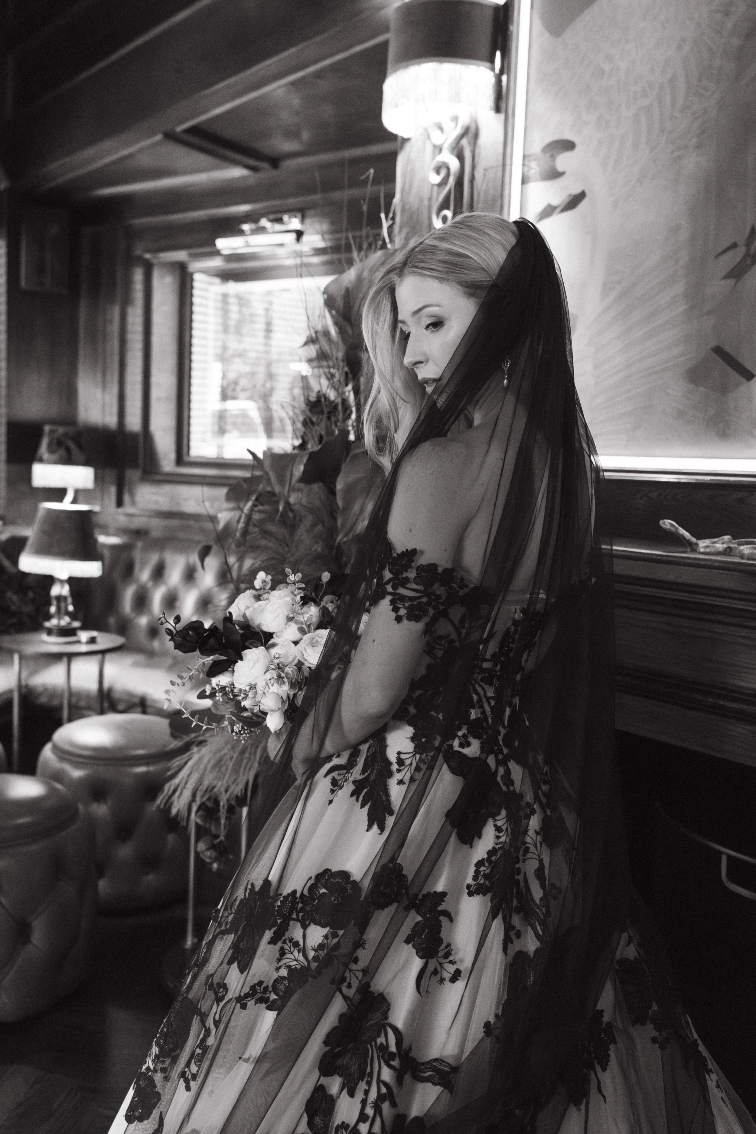 A woman in a wedding dress holding a bouquet of flowers, standing indoors near a window and a wooden wall. - captured by an Edinburgh wedding photographer