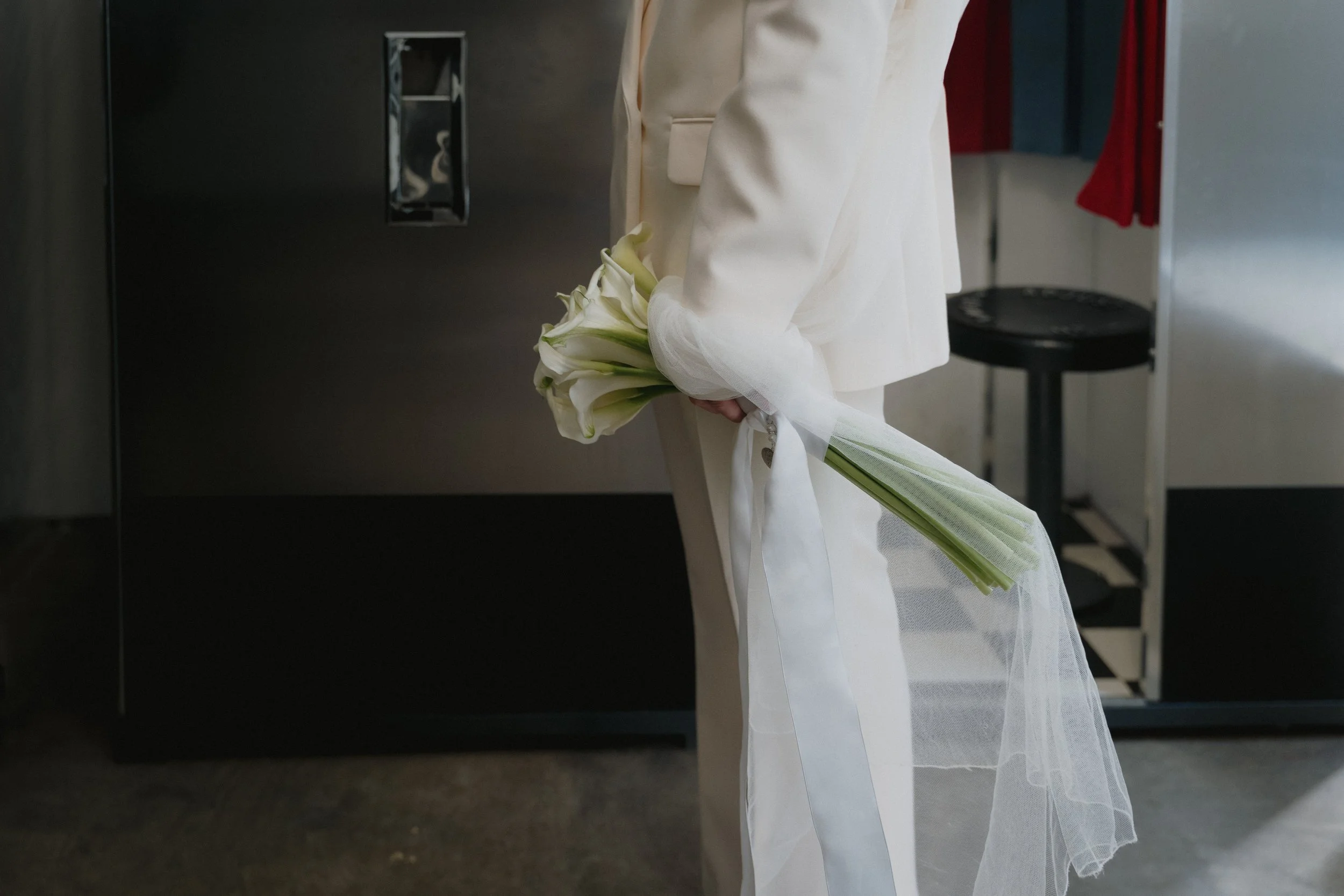 A person dressed in a white suit holding a bouquet of white calla lilies, with the flowers wrapped in white tulle. - captured by an Edinburgh wedding photographer