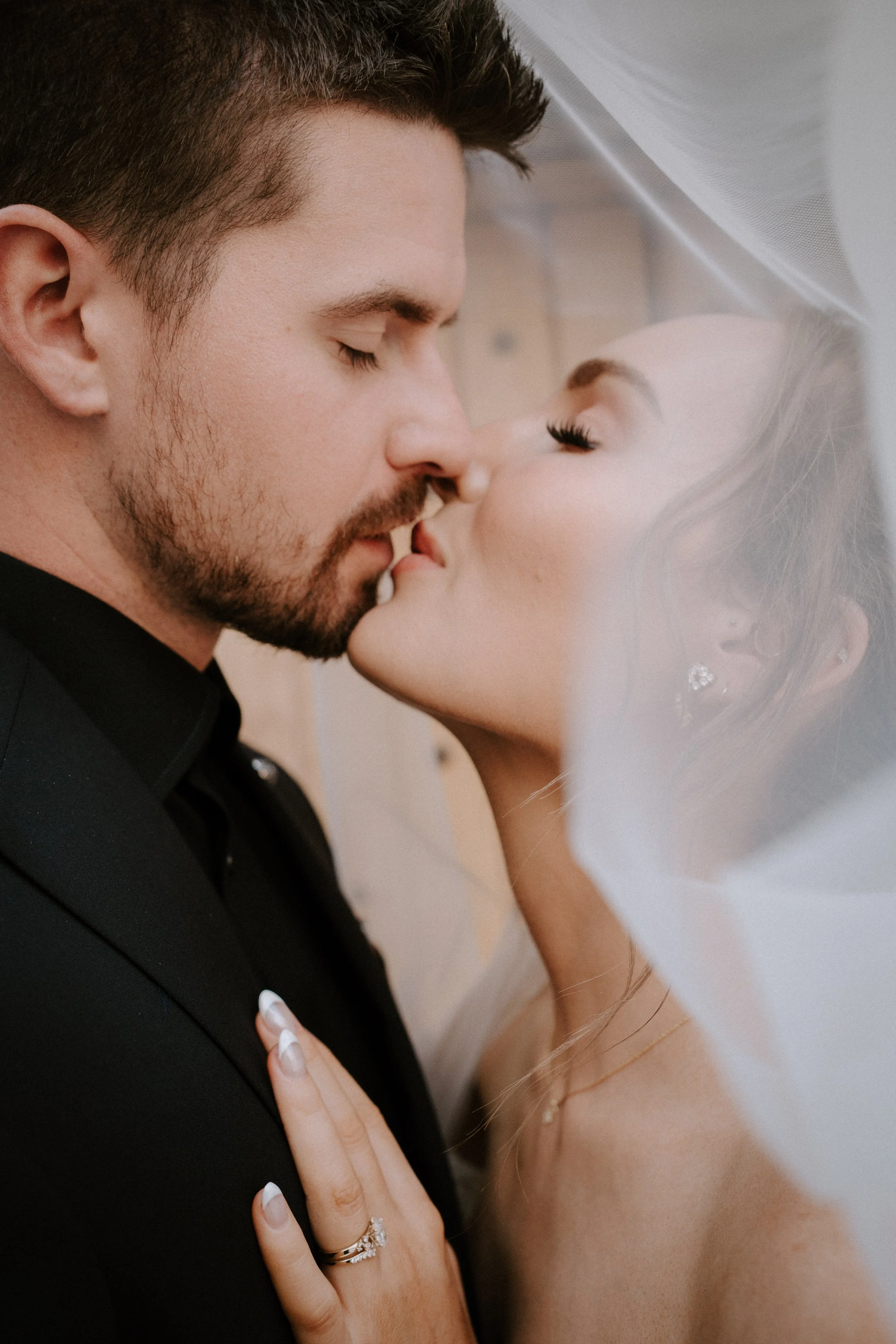 A bride and groom sharing a kiss, with the bride wearing a wedding dress and veil, and the groom dressed in a black suit. - captured by an Edinburgh wedding photographer