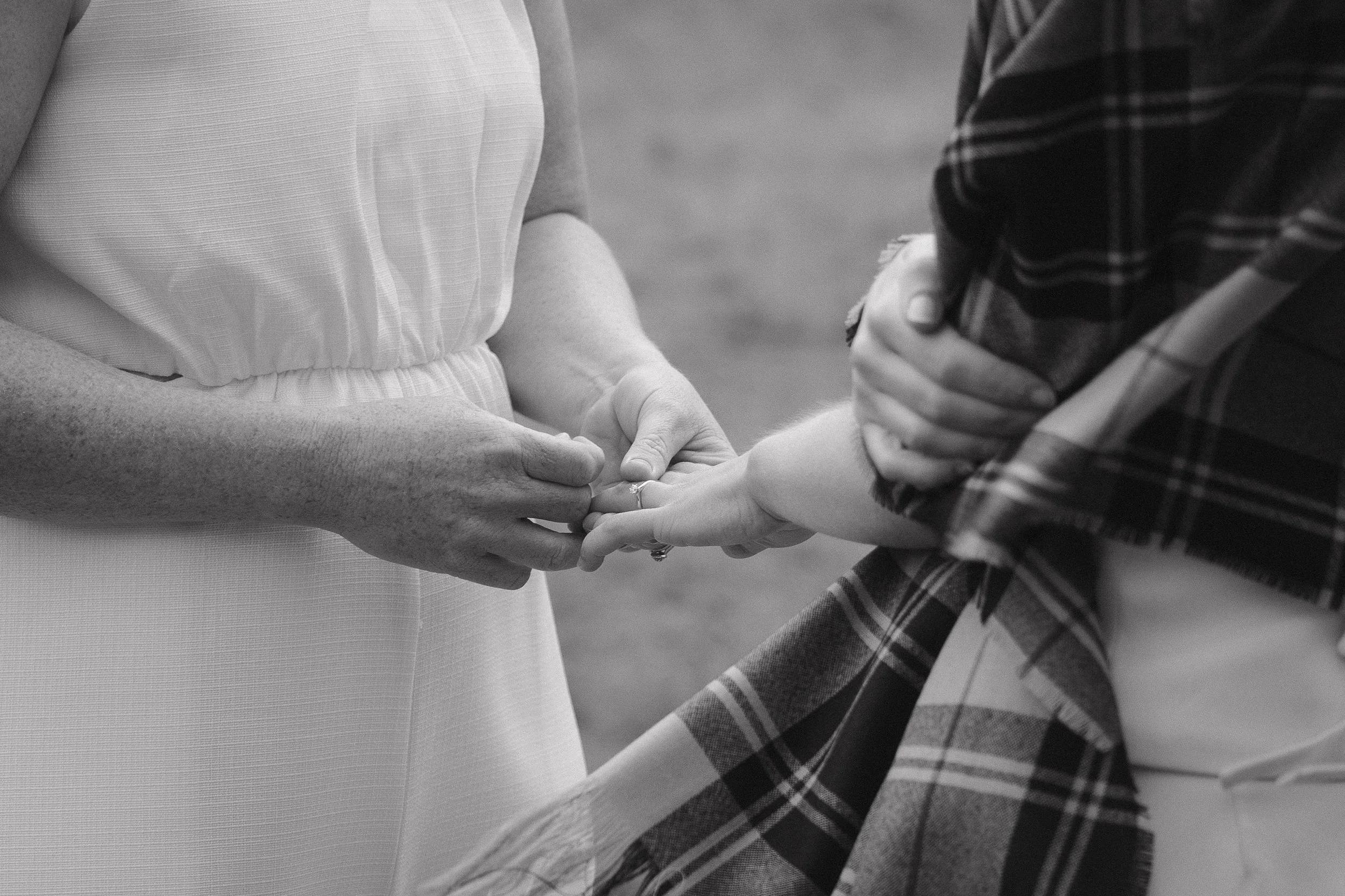 A person is holding and placing a ring on another person's finger during a wedding or engagement ceremony, both are standing close together.