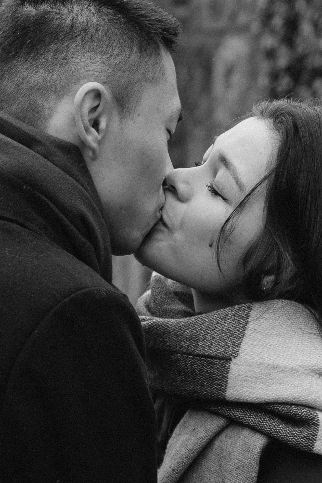 A black-and-white photo of a couple kissing with eyes closed, wrapped in a plaid scarf - captured by an Edinburgh wedding photographer