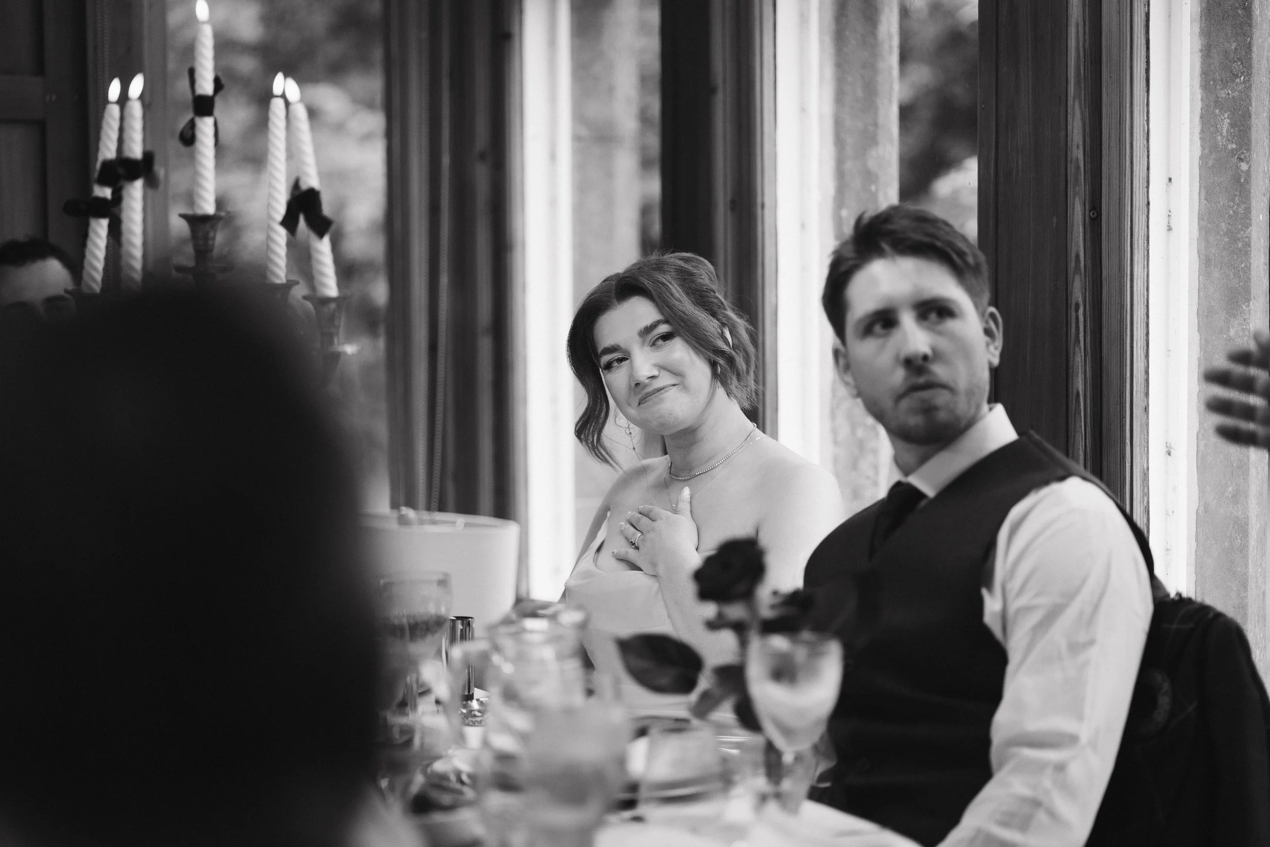 A black-and-white photo of a woman and man sitting at a dining table during a formal event, with a candelabra in the background. - captured by an Edinburgh wedding photographer
