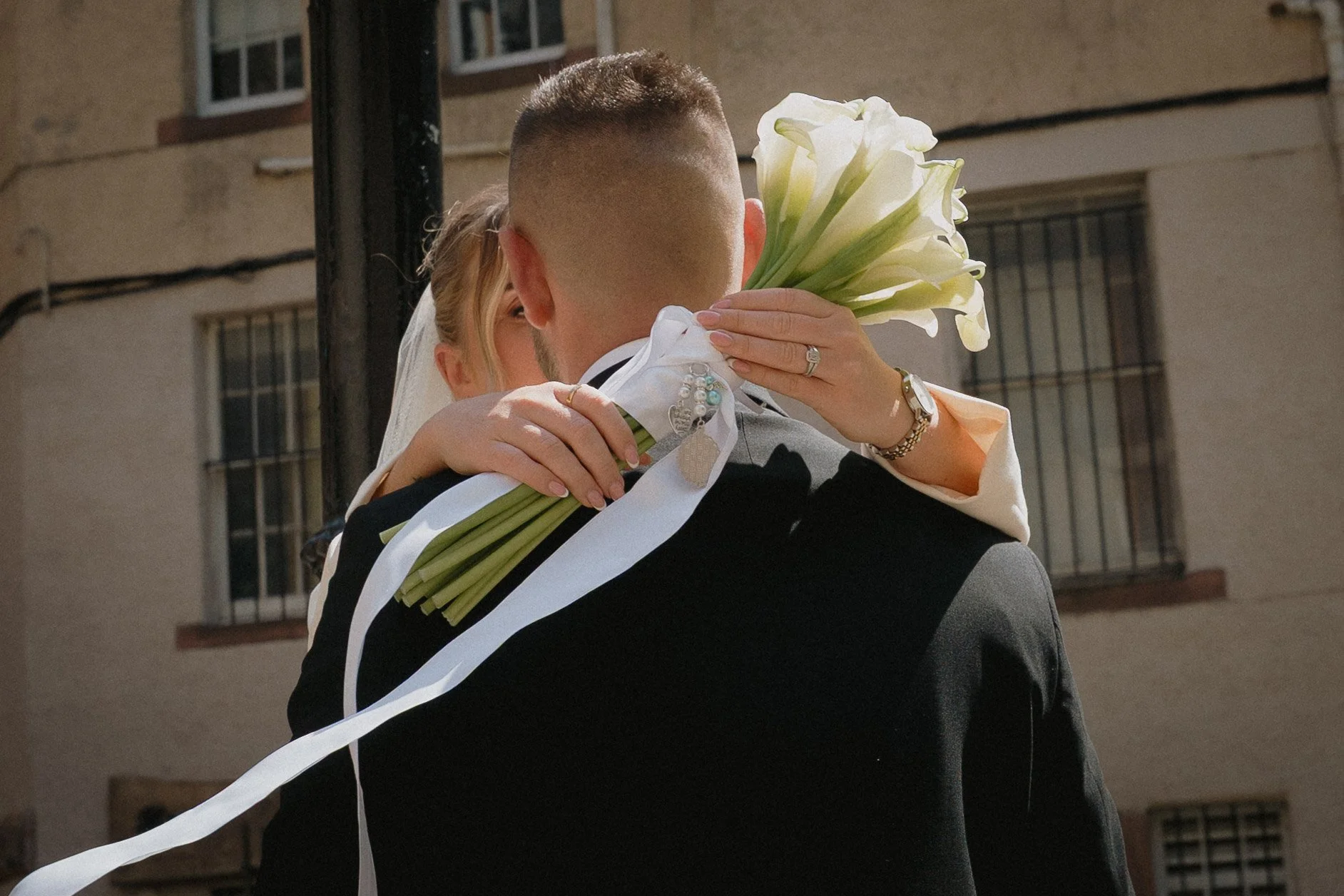 A bride and groom embrace outdoors, with the bride holding a bouquet of white calla lilies, during a wedding celebration. - captured by an Edinburgh wedding photographer