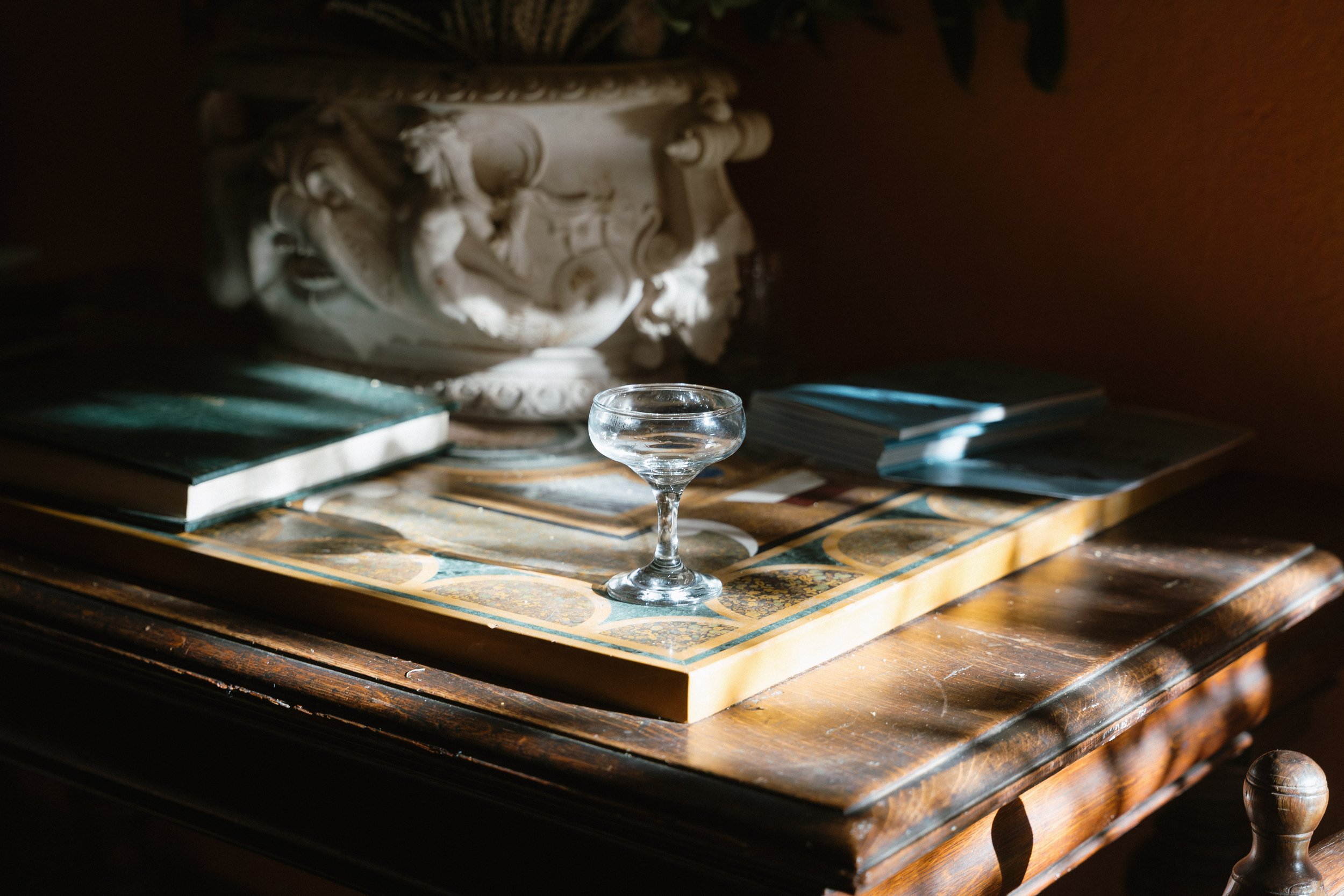 A wooden table with a decorative top, holding a small glass filled with water, a stack of opened books, and a large ornate white ceramic vase with floral designs. - captured by an Edinburgh wedding photographer