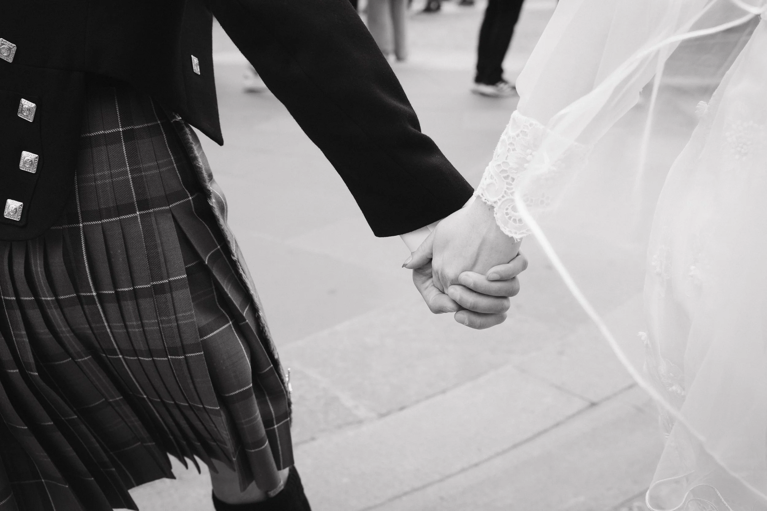 People holding hands, one in a kilt and the other in a lace wedding dress. - captured by an Edinburgh wedding photographer