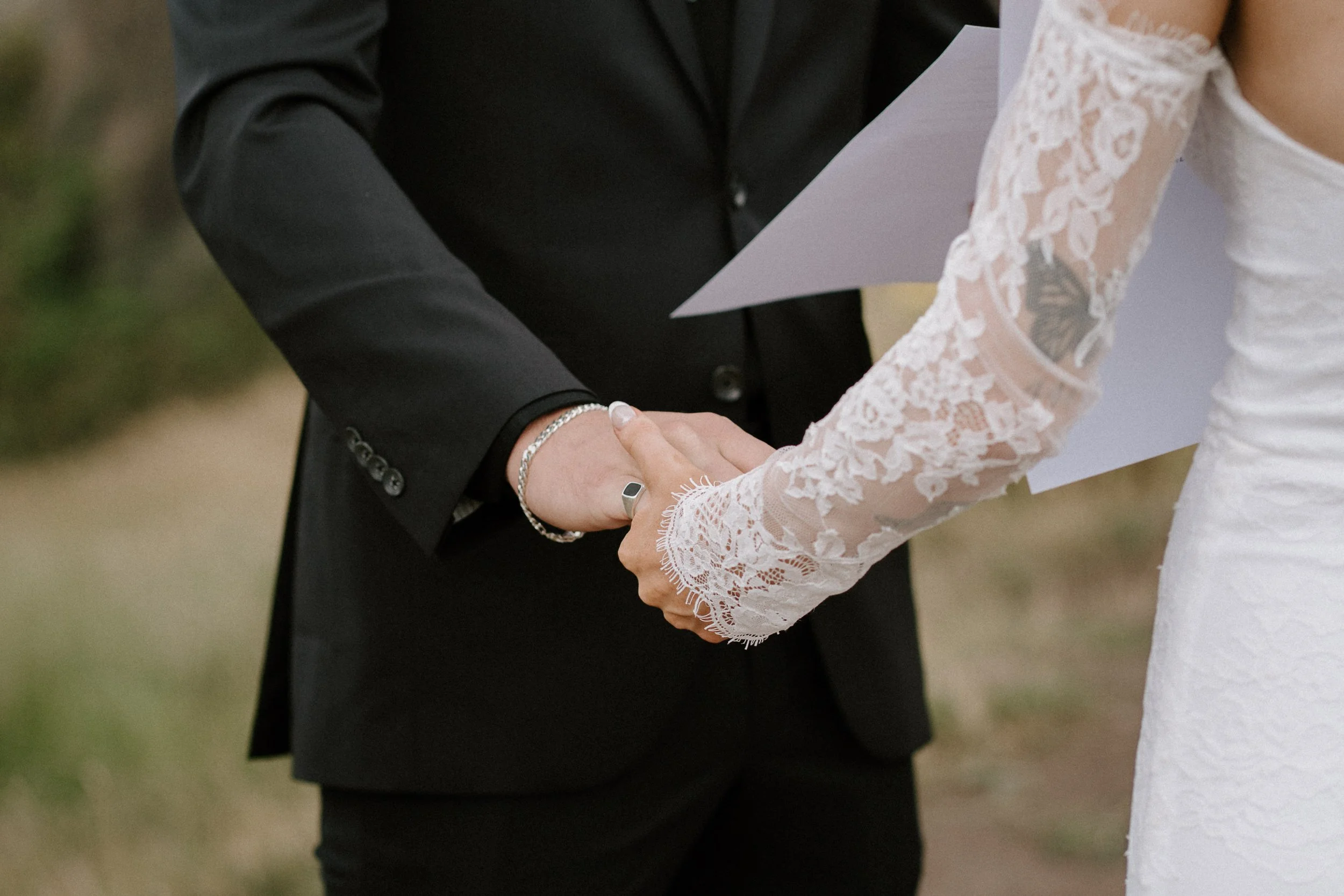 A close-up of a couple holding hands during a wedding ceremony, with the groom wearing a black suit and the bride in a lace wedding dress. - captured by an Edinburgh wedding photographer