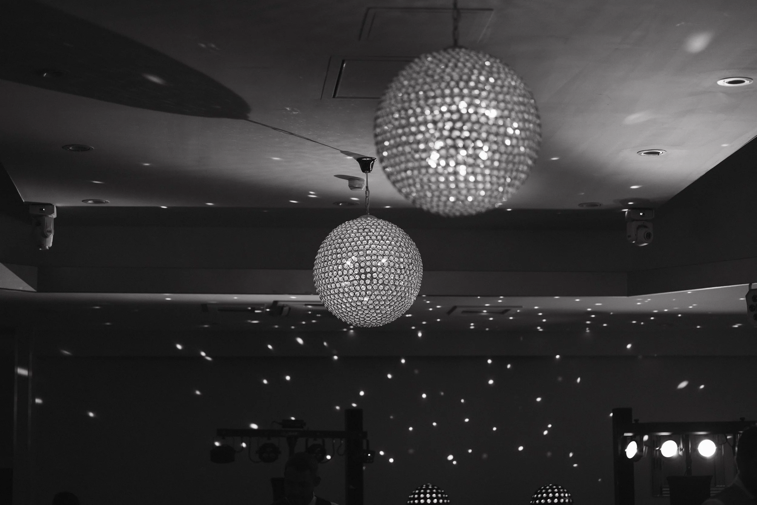 Two large spherical chandeliers hanging from a ceiling in a dark room, with small light reflections creating patterns on the ceiling and walls. - captured by an Edinburgh wedding photographer