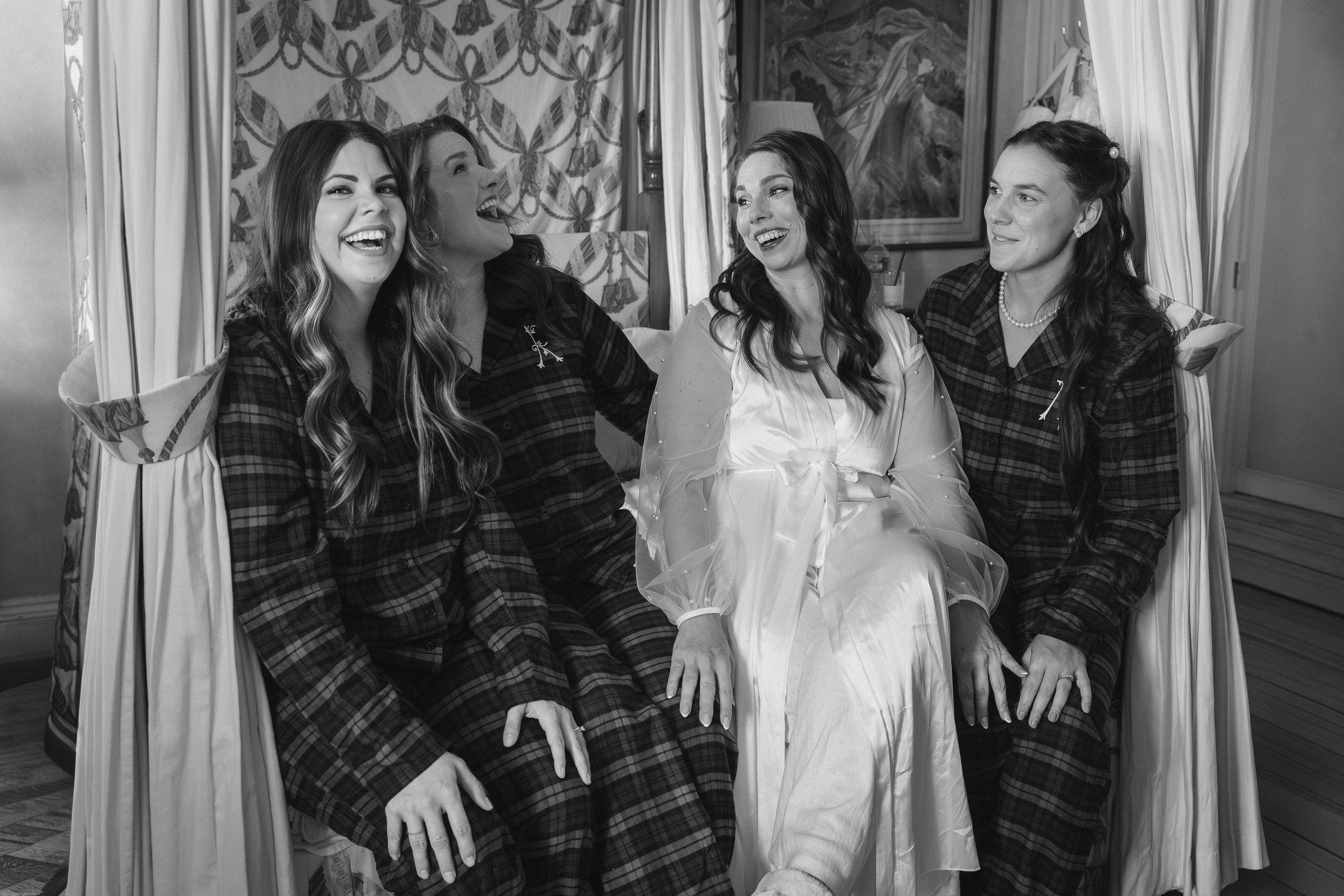 Four women sitting together, dressed in pajamas, laughing and smiling. - captured by an Edinburgh wedding photographer