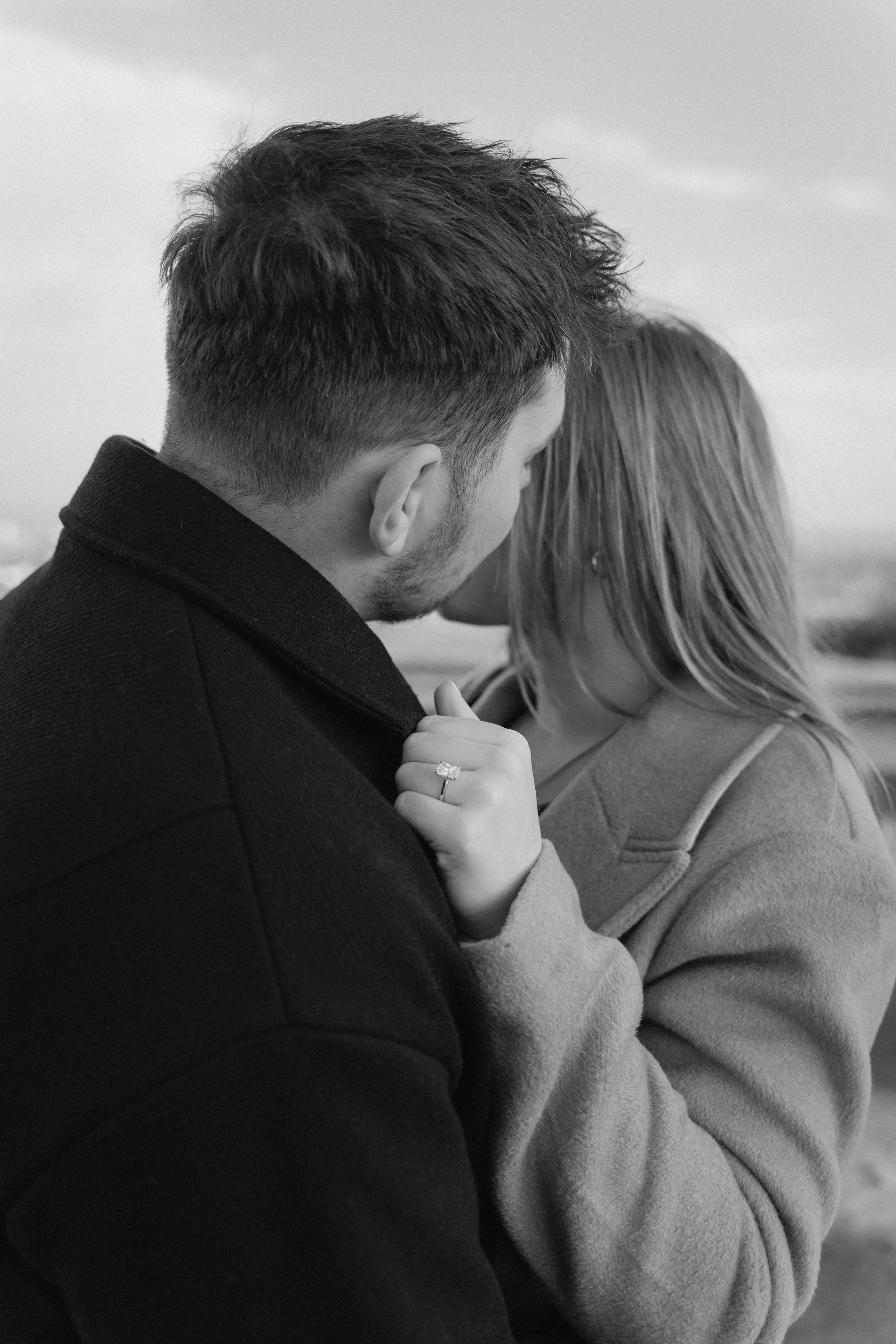 A couple close together, with their foreheads touching. The man's back is to the camera, and the woman's face is partially visible with her hand resting on his chest, showing an engagement ring. - captured by an Edinburgh wedding photographer