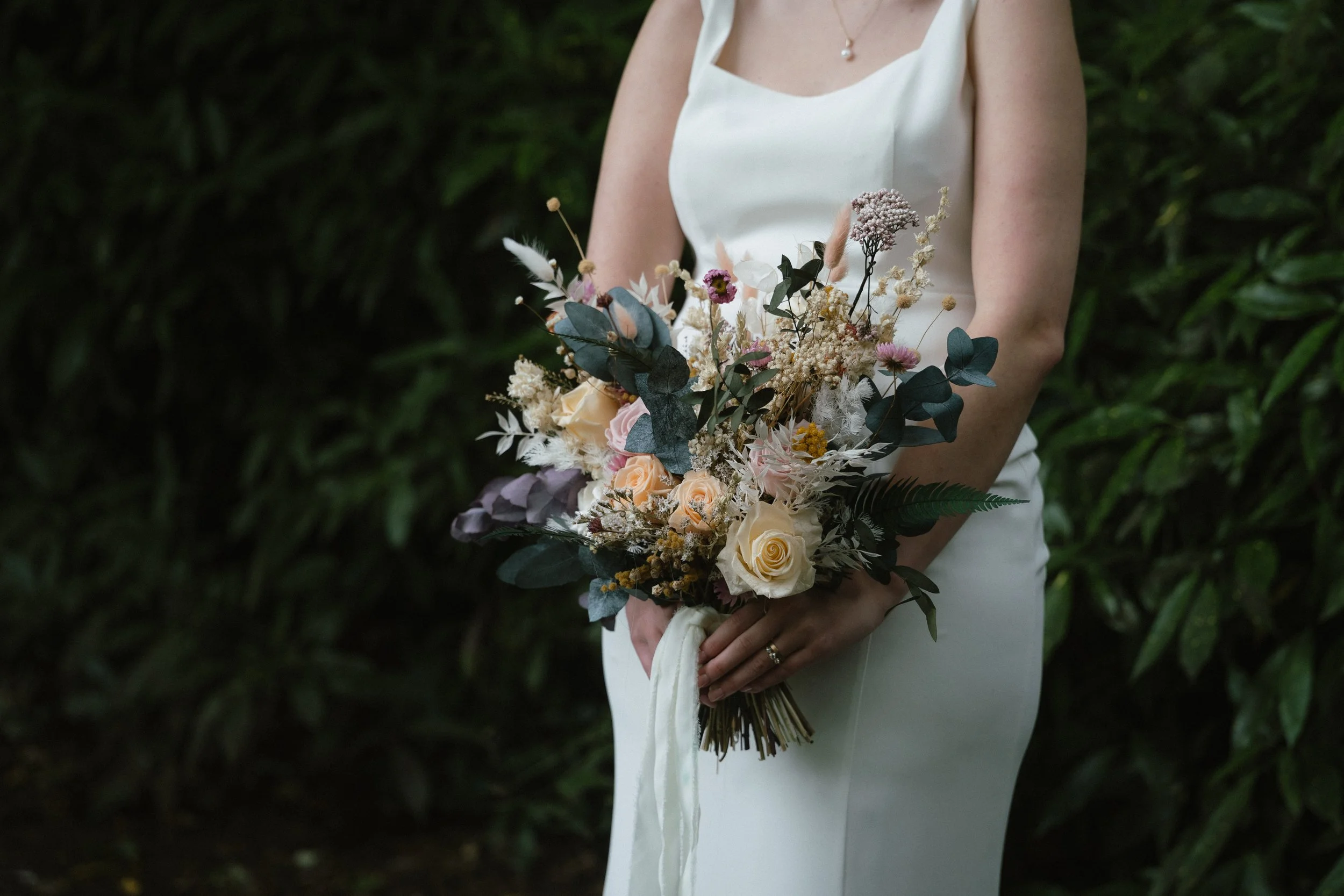 A woman in a white dress holding a bouquet of mixed flowers including roses and greenery outdoors.