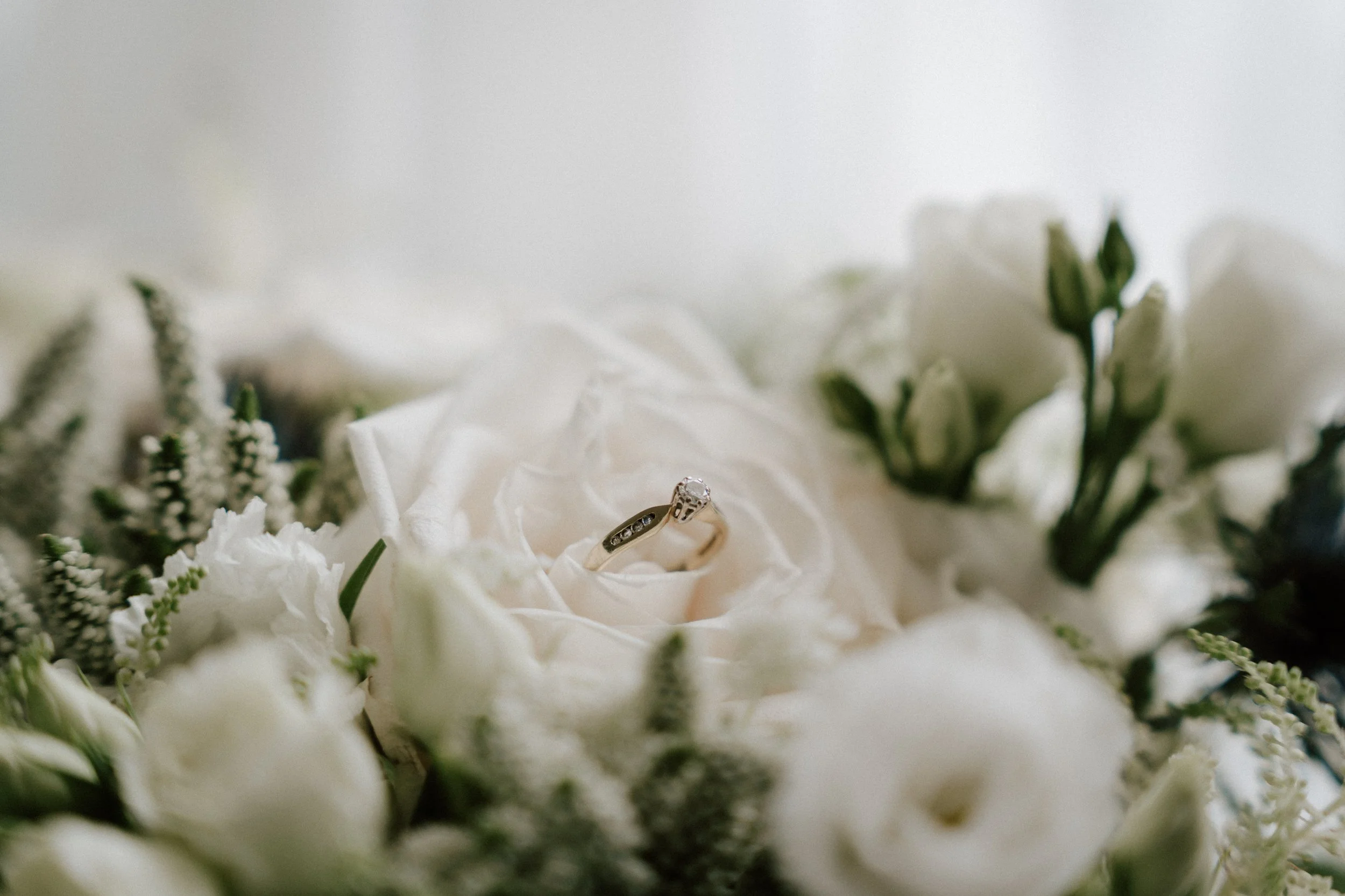 A wedding ring on a white rose surrounded by other white flowers and greenery. - captured by an Edinburgh wedding photographer