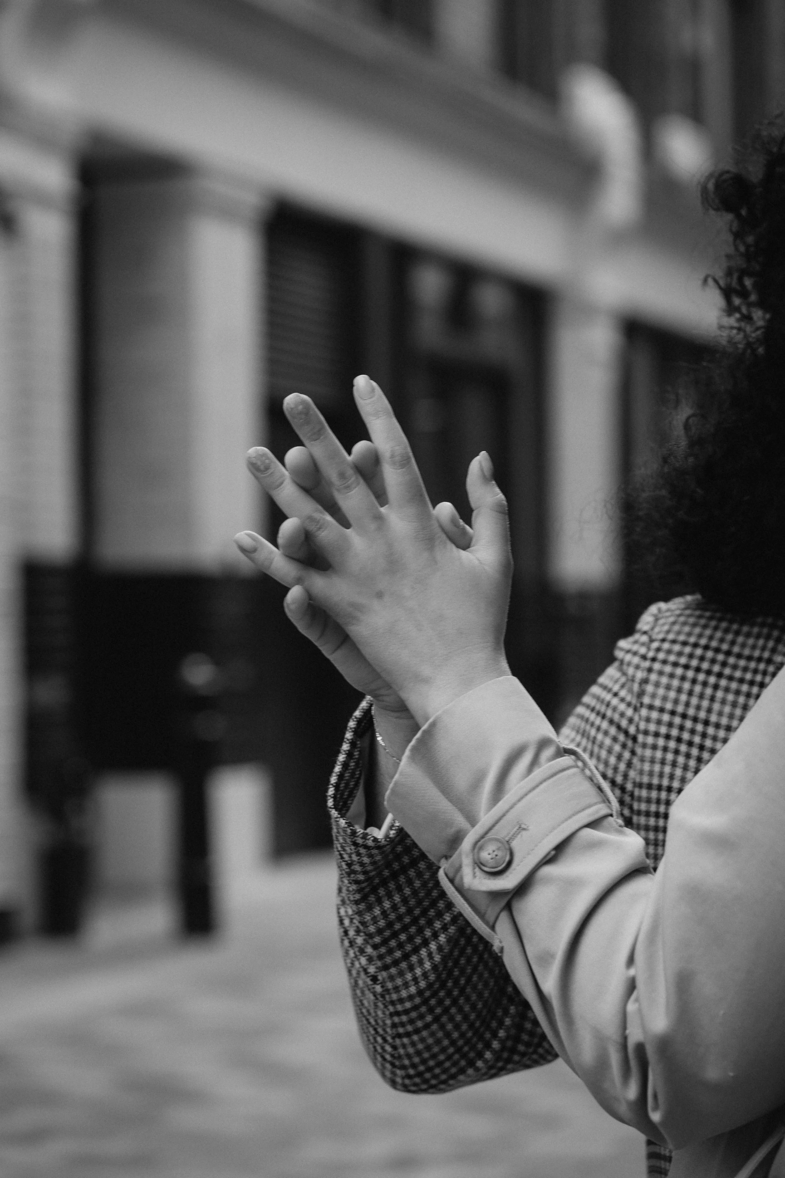 A woman with curly hair claps her hands together on a city street in black and white - captured by an Edinburgh wedding photographer