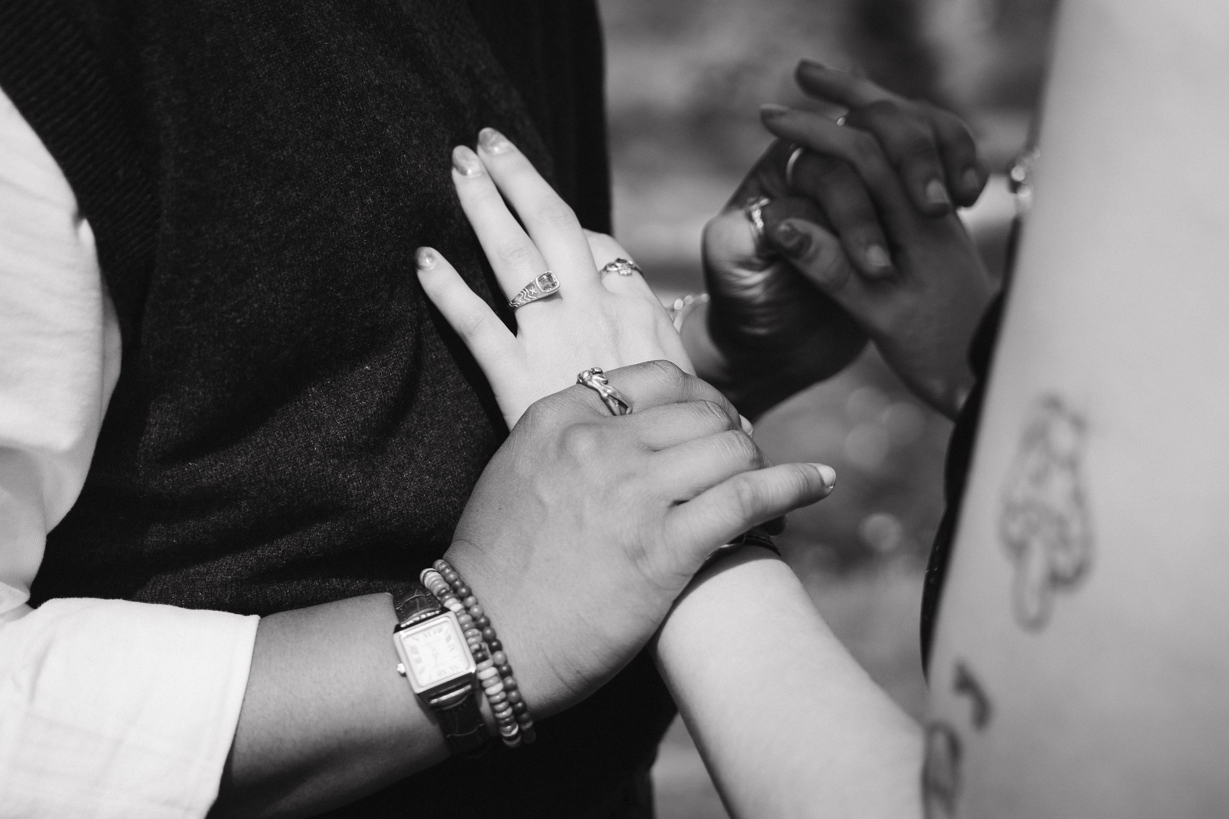 A couple holding hands during a wedding ceremony, with both wearing wedding rings. One person wears a watch and beaded bracelet, the other's hand has rings and nail polish. - captured by an Edinburgh wedding photographer