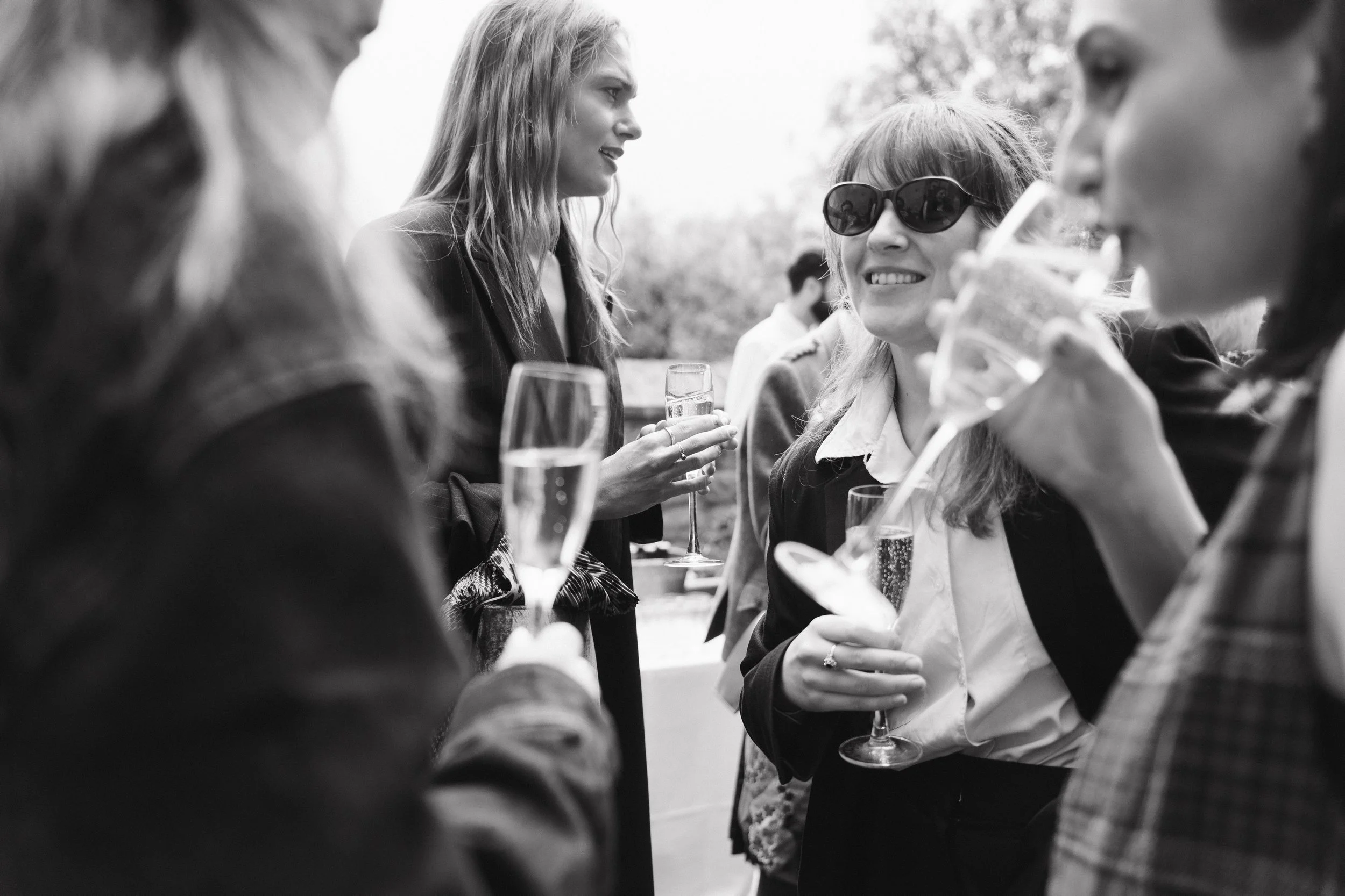 Group of women at an outdoor gathering, holding glasses of champagne and chatting, in black and white. - captured by an Edinburgh wedding photographer