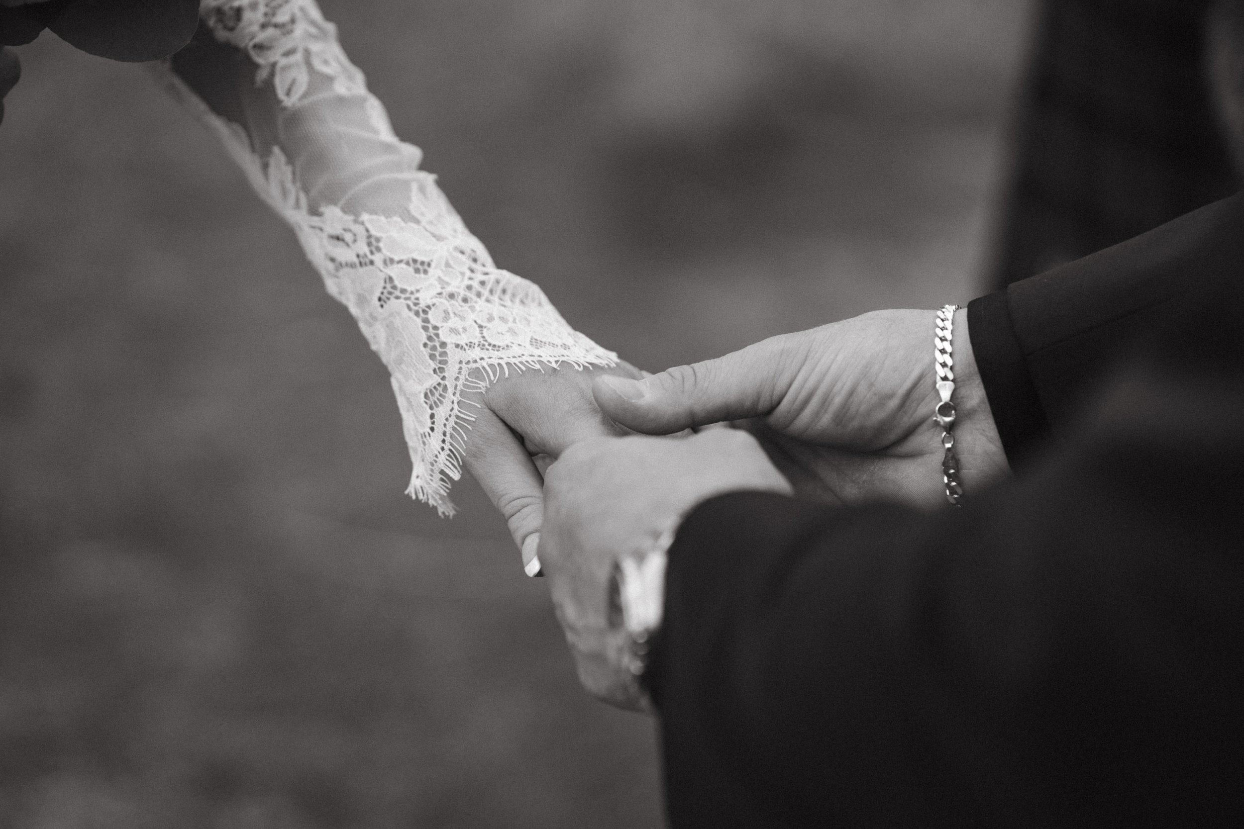 A close-up of a couple holding hands during a wedding ceremony, with the woman wearing a lace wedding dress and the man in a dark suit. - captured by an Edinburgh wedding photographer
