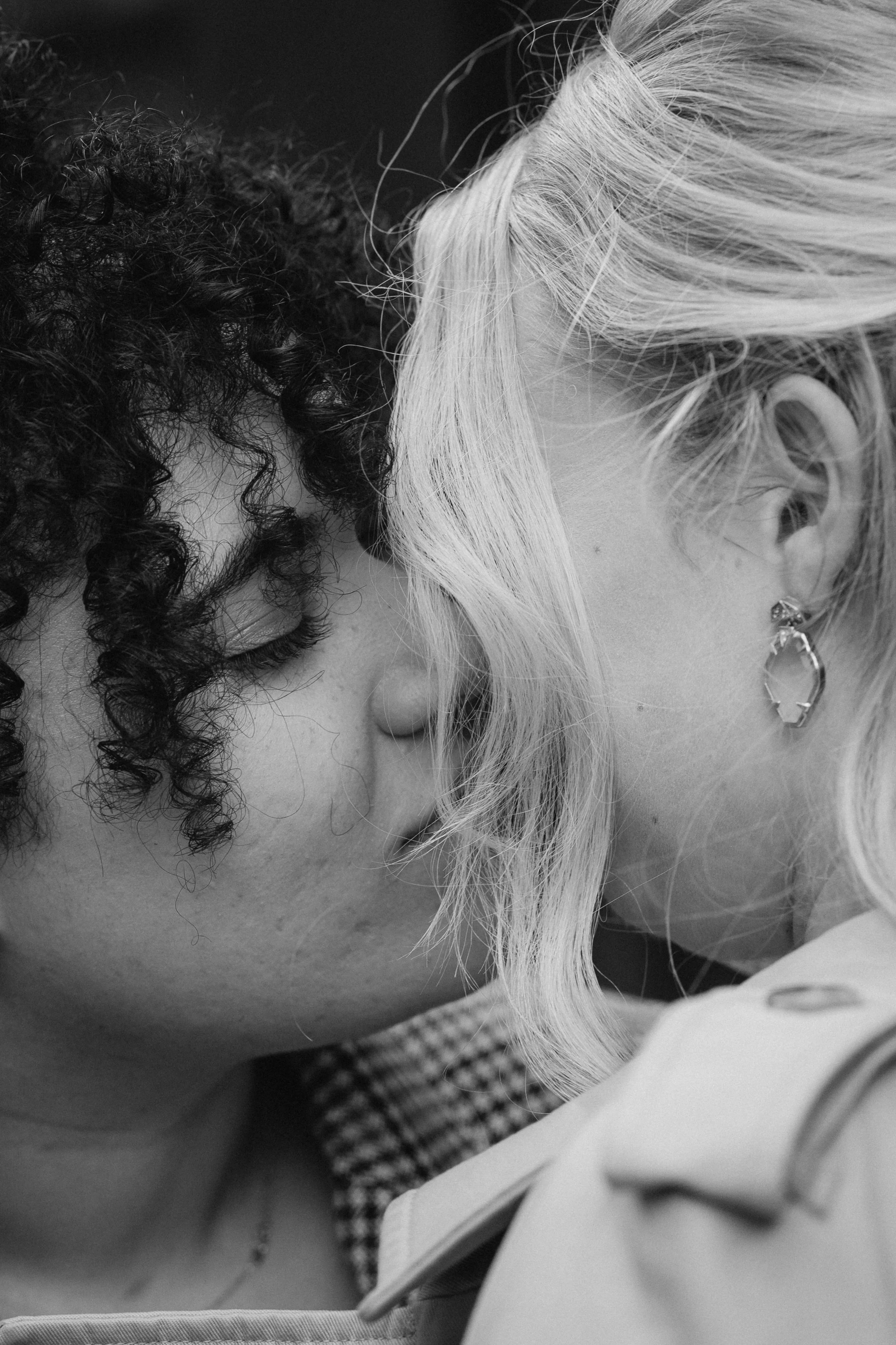 Close-up of two women with their foreheads touching, eyes closed, in an intimate moment, one with curly dark hair and the other with straight blonde hair and earrings - captured by an Edinburgh wedding photographer