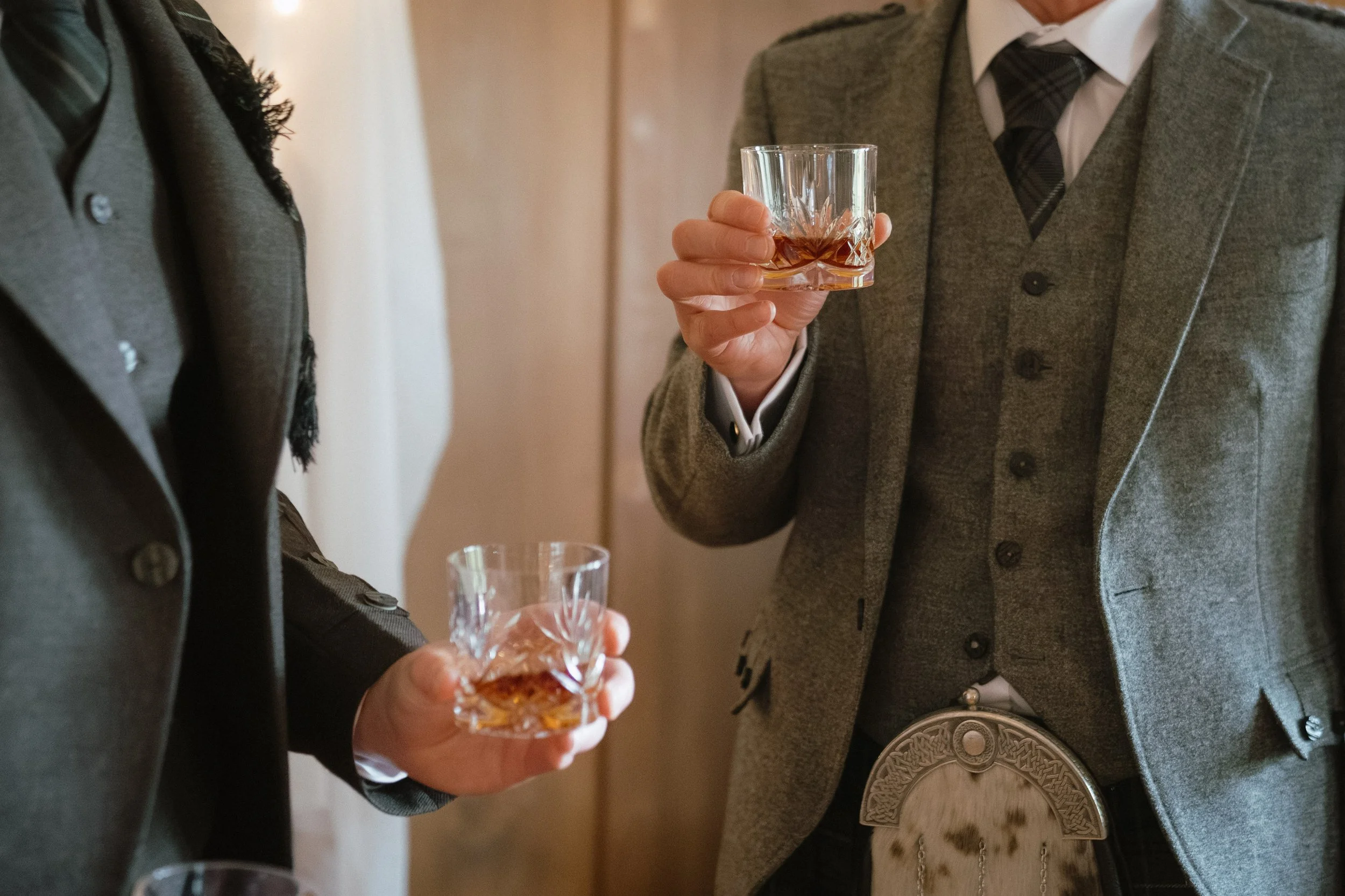 Two people in formal attire holding glasses of whiskey during a toast. - captured by an Edinburgh wedding photographer