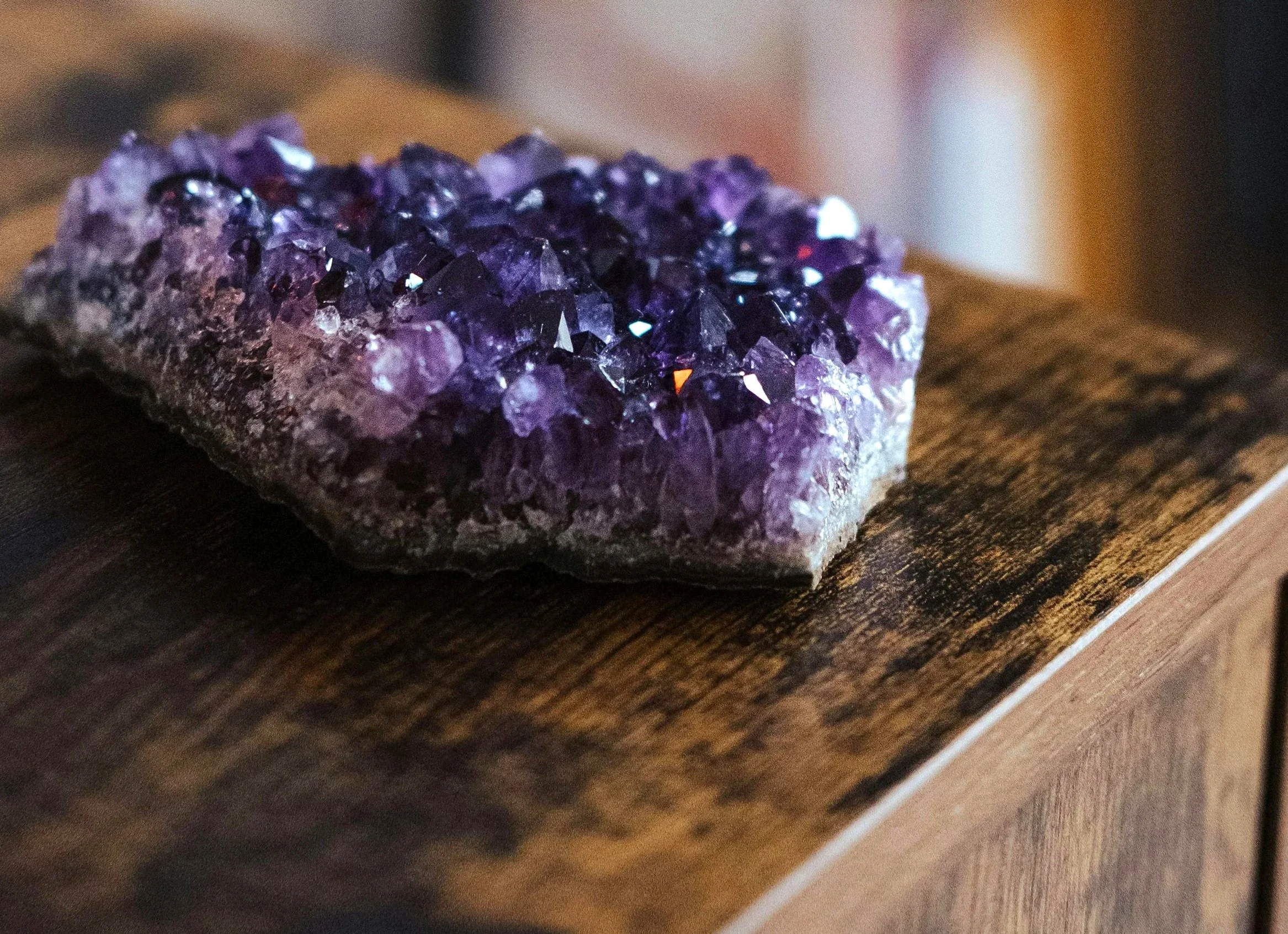 Un amas d'améthyste d'un violet profond posé sur une table en bois aux teintes chaudes, invitant à la réflexion et à l'introspection.