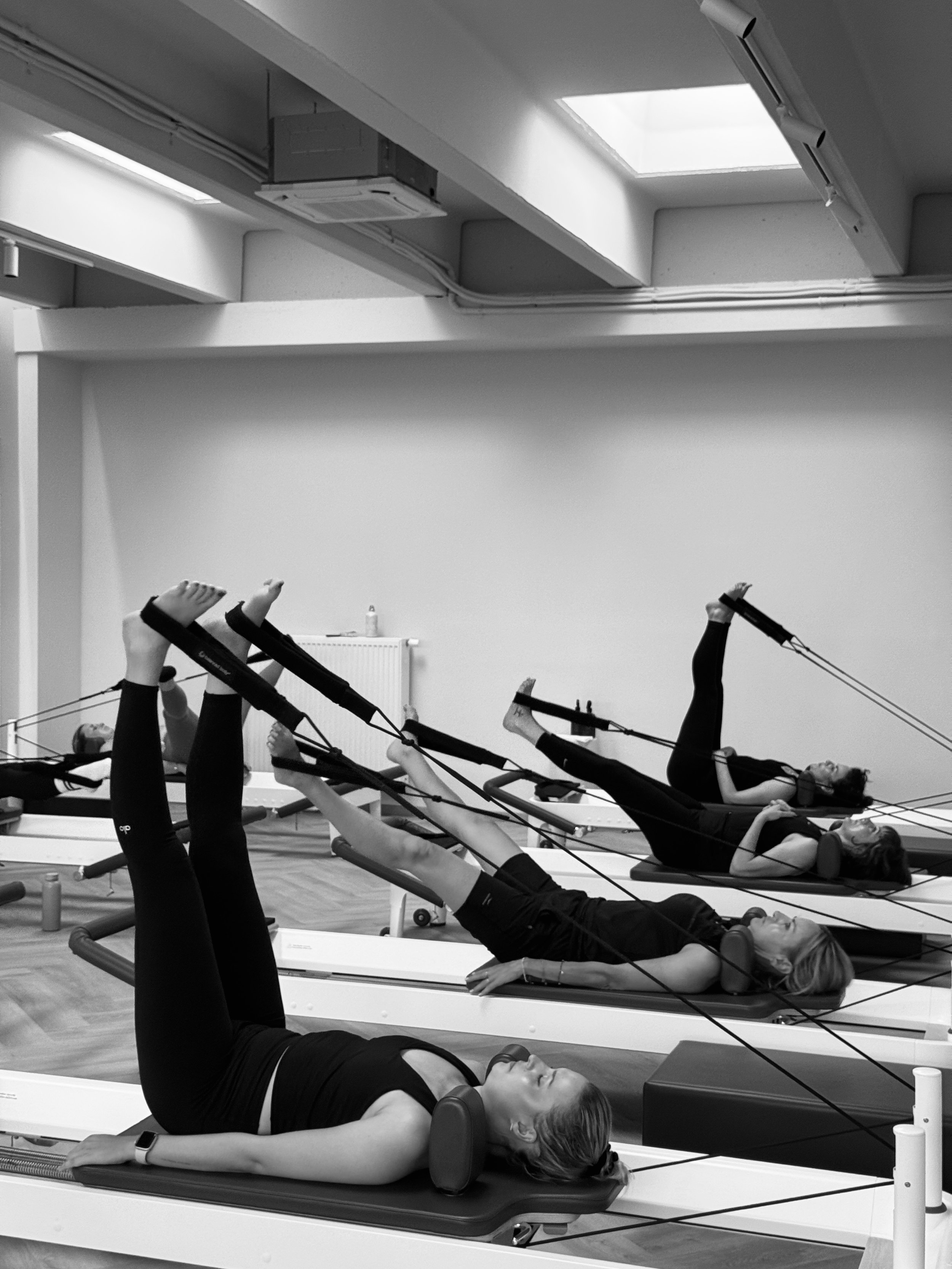 Frauen beim Pilates-Training auf Pilates-Reformer in einem Fitnessstudio, schwarz-weiß.