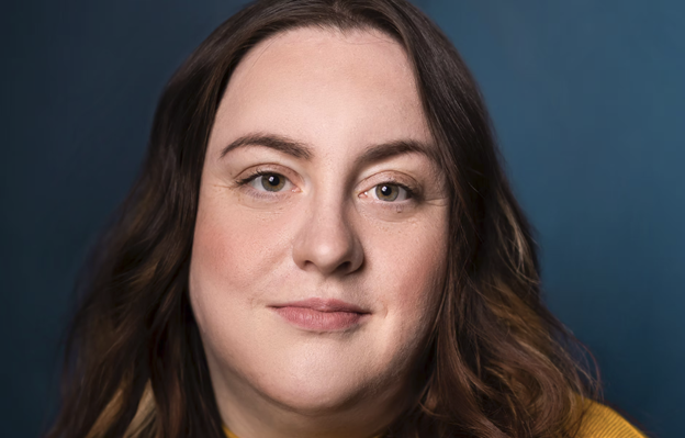 A photograph portrait of Carly Neis with brown hair and brown eyes, wearing a yellow sweater top.