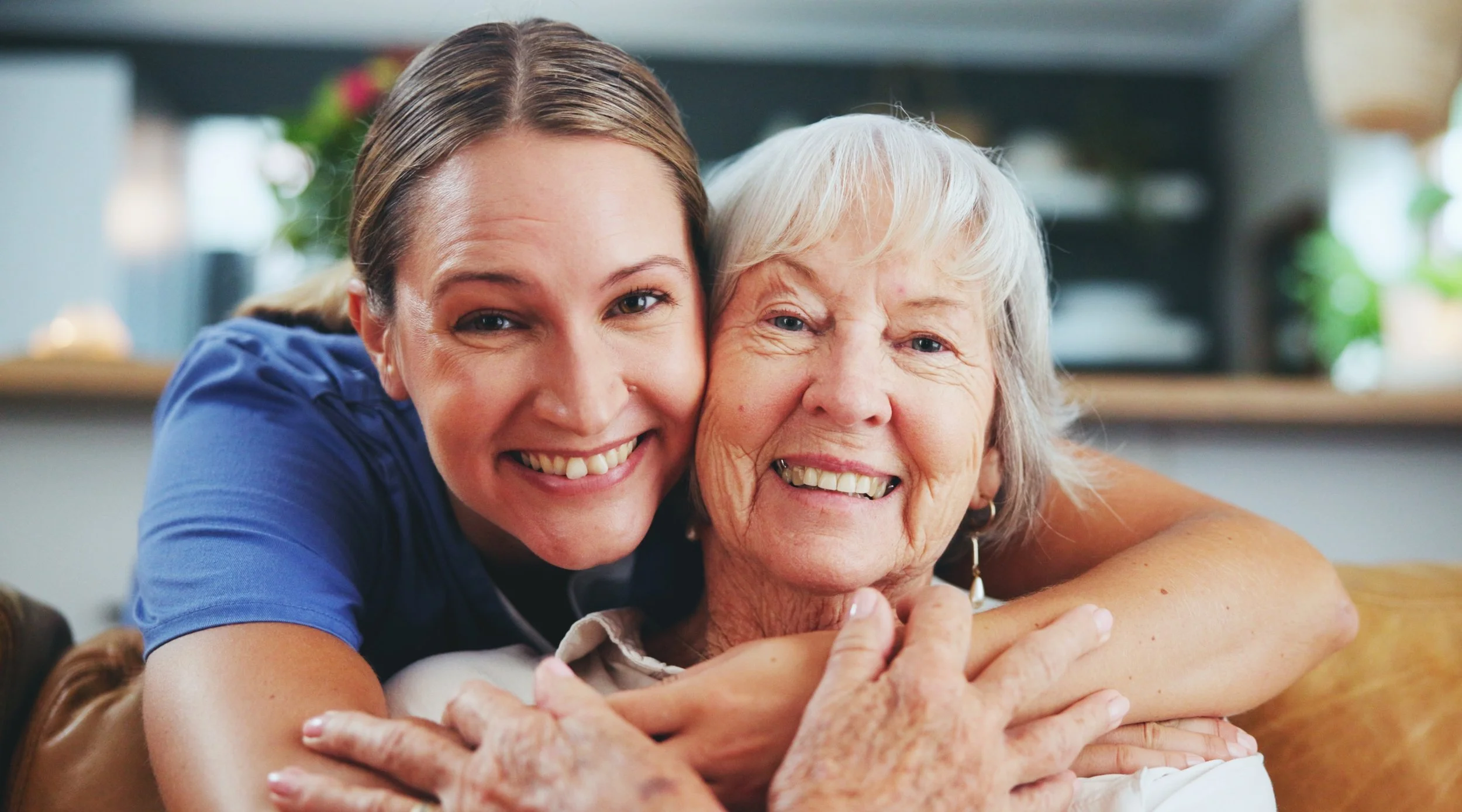A young woman hugging an elderly woman with a big smile.