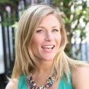 A woman with blonde hair smiling outdoors, wearing a green top and a turquoise necklace.