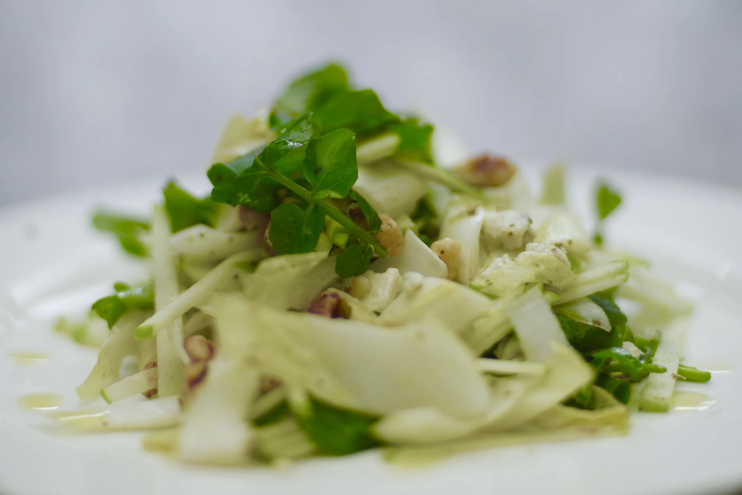 Close-up of a fresh cabbage slaw salad garnished with green herbs and chopped nuts on a white plate.