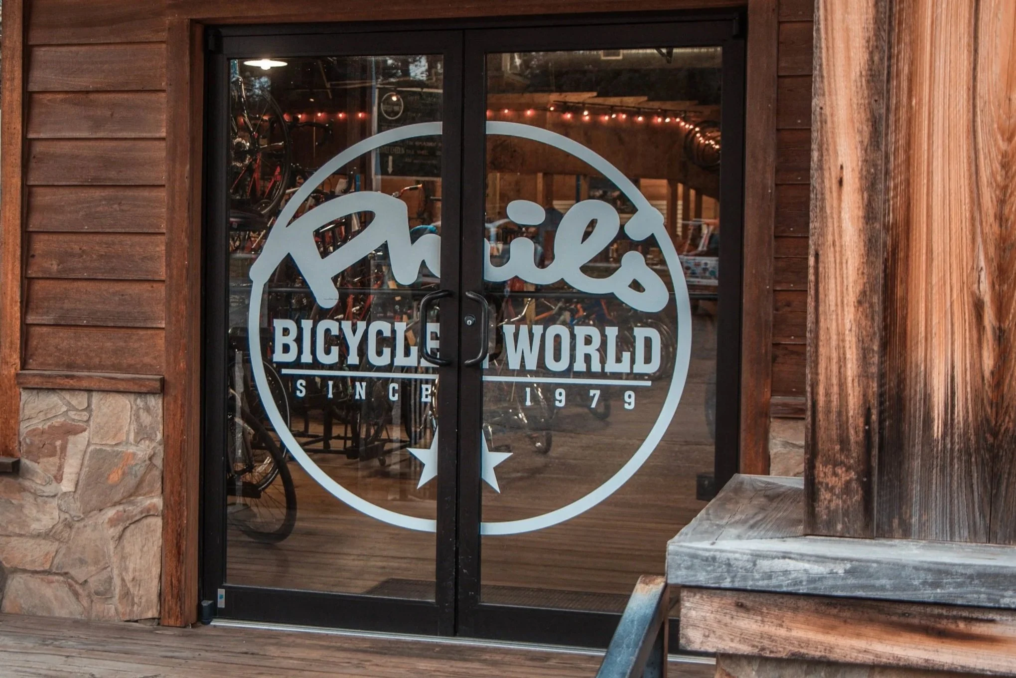The glass door of a bicycle shop with the logo 'Phil's Bicycle World, since 1979' printed on it, and bicycles are visible inside.
