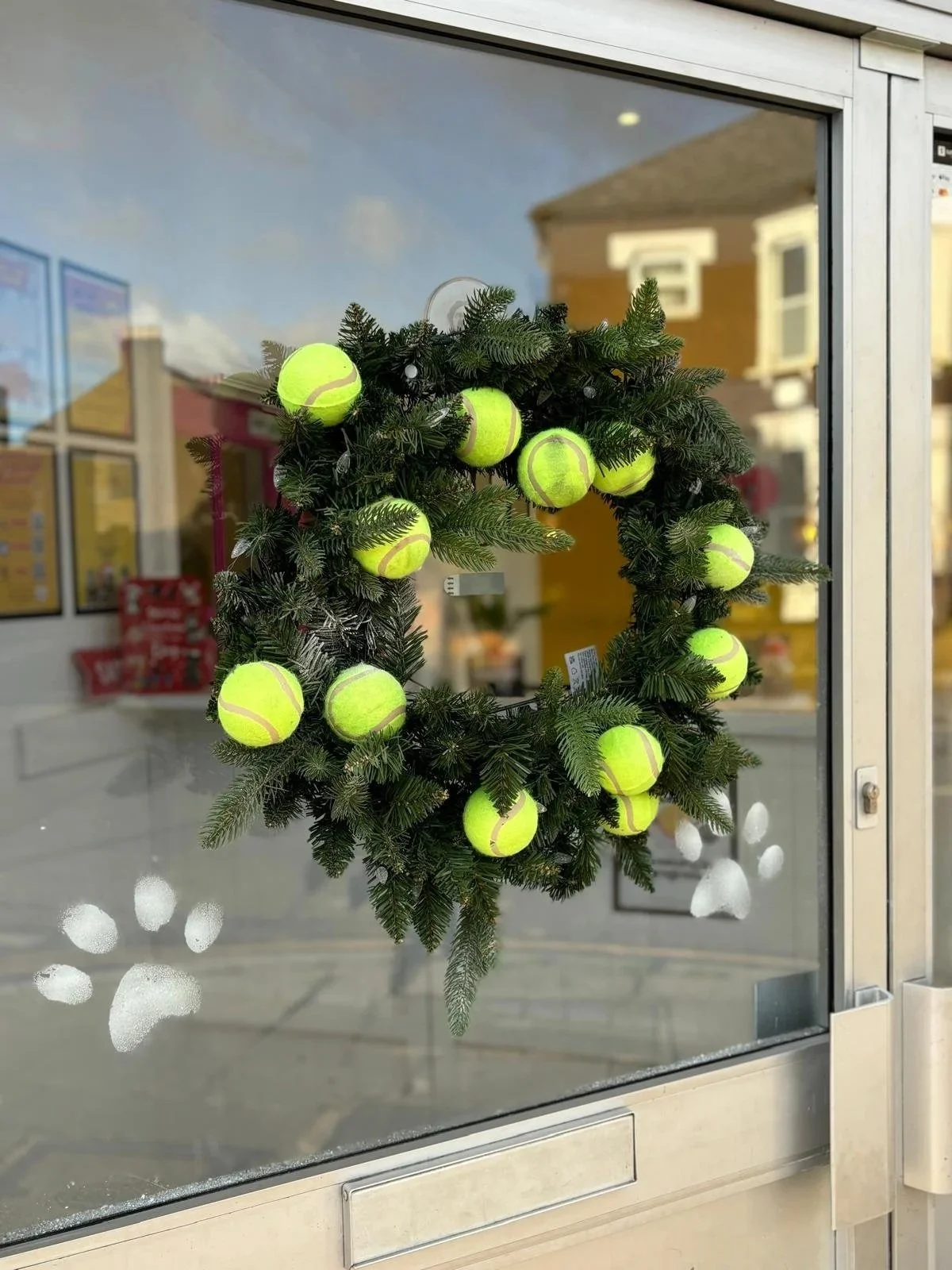A wreath decorated with tennis balls hanging on a glass door, with some paw prints painted on the glass.