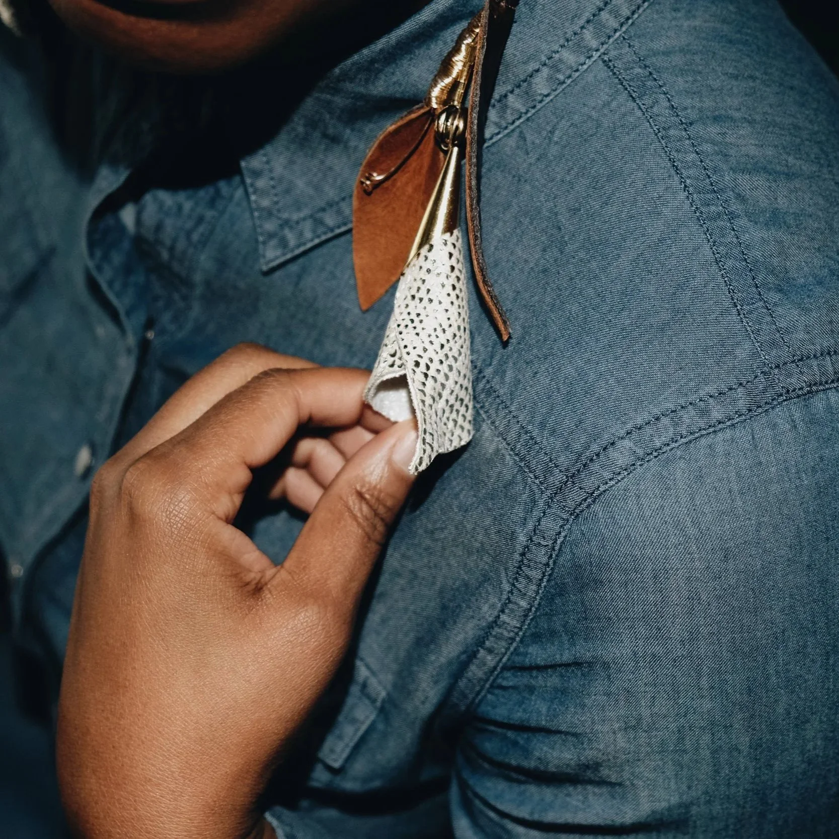 Person pinning a beaded necklace to a denim shirt on their chest.