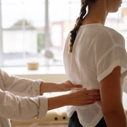 A person receiving a back adjustment or massage from another person in a bright room with large windows.
