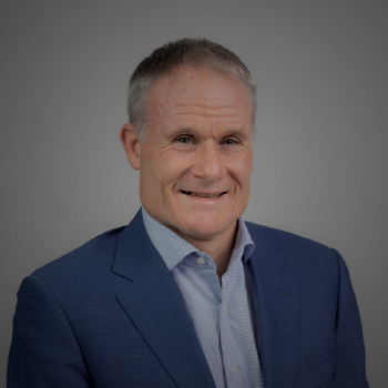 Portrait of a smiling middle-aged man in a blue suit and light blue shirt against a gray background.