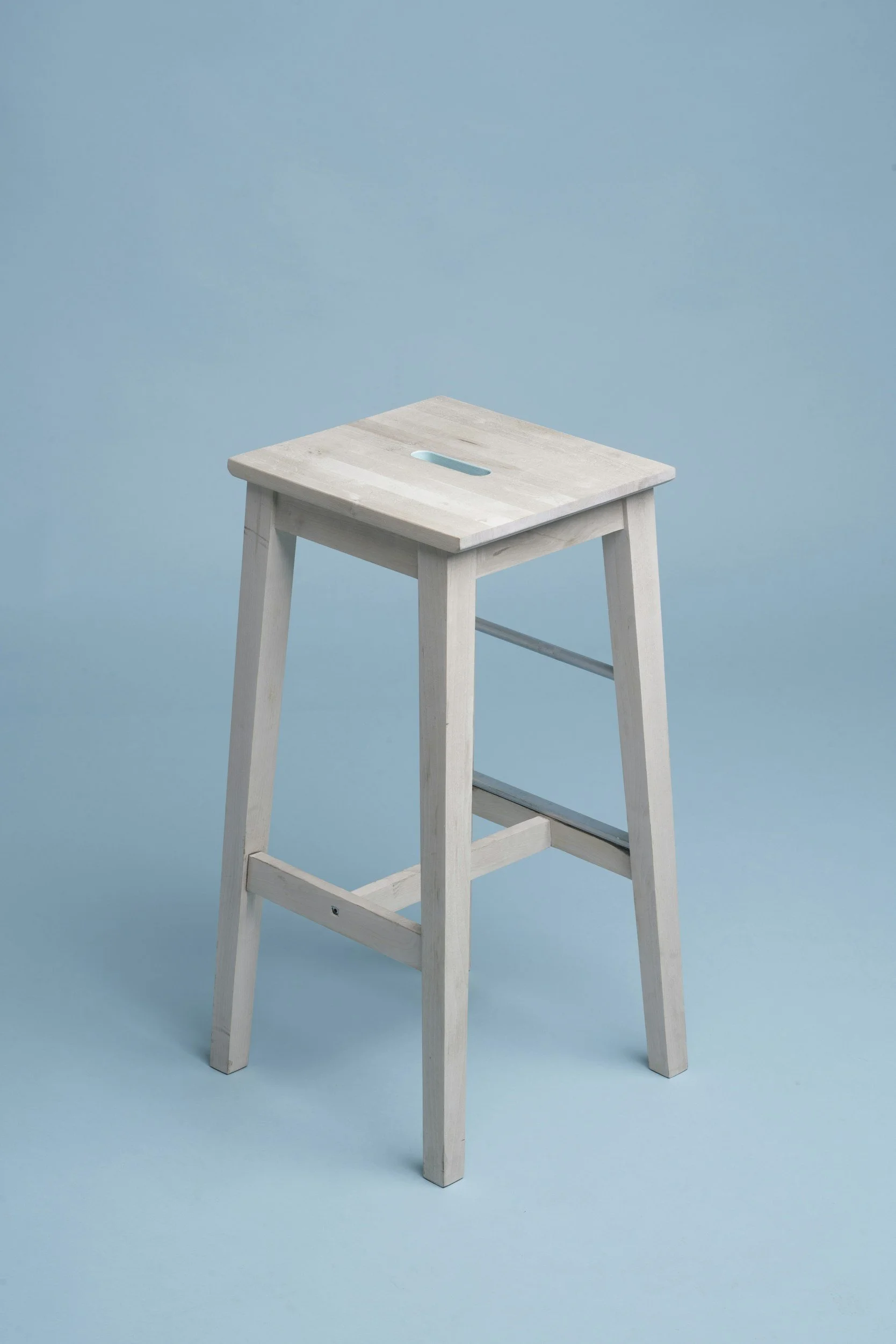 Minimal white wooden stool against a soft blue background, representing Studio Hosten’s calm, hosting-focused interior design approach. Minimalism, timeless, high-end materials, wooden furntiure.