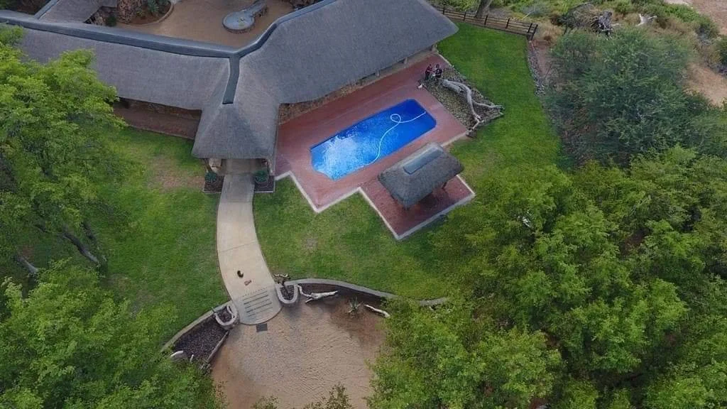 Aerial view of a house with a swimming pool, surrounded by trees and a lawn.
