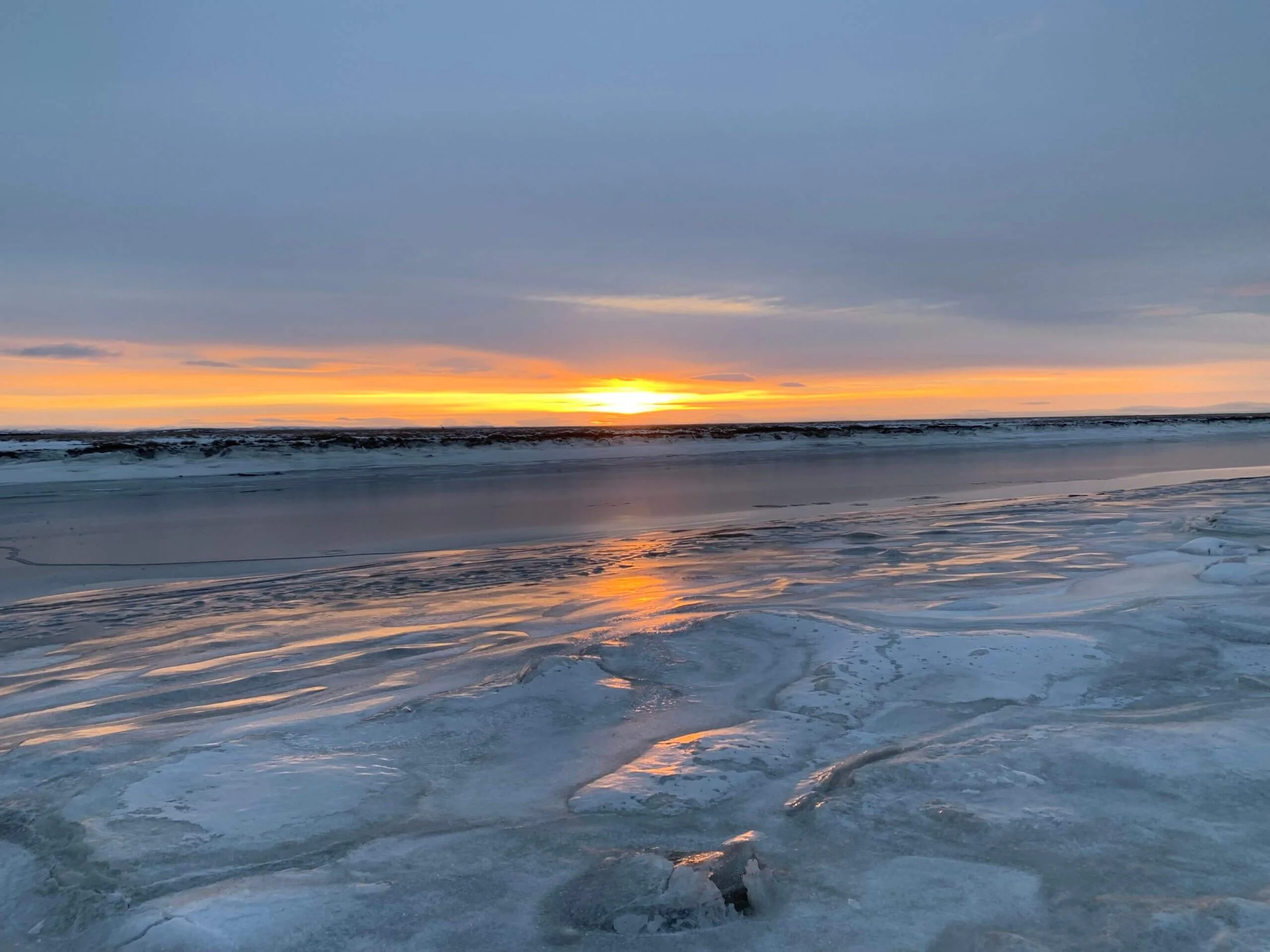 A white pickup truck driving along a rugged dirt path through a vast, dry African landscape with sparse bushes and trees stretching toward the horizon.