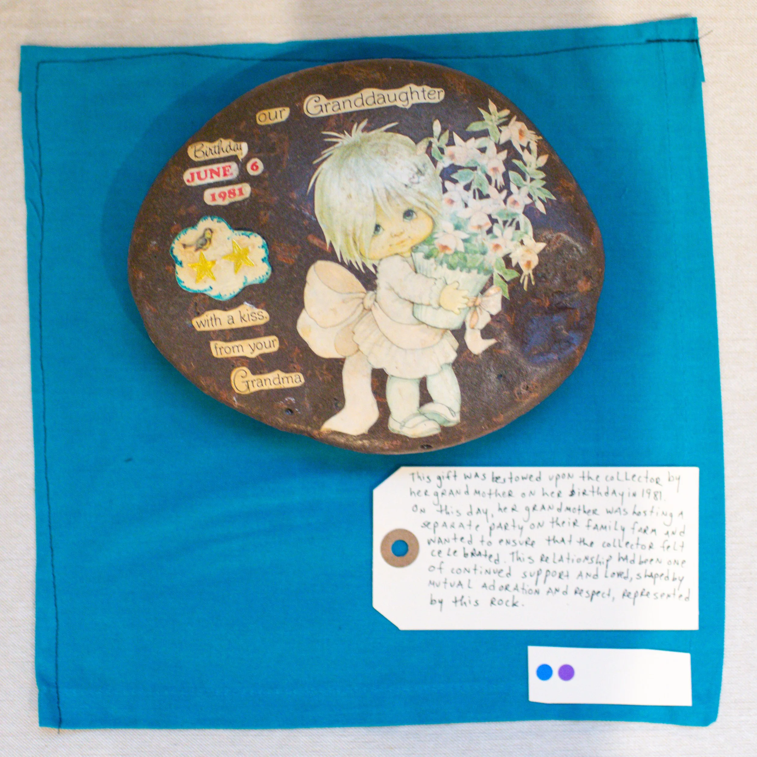 Decorative stone with a drawing of a young girl holding a bouquet of flowers, birthday details, and a written note on blue background.