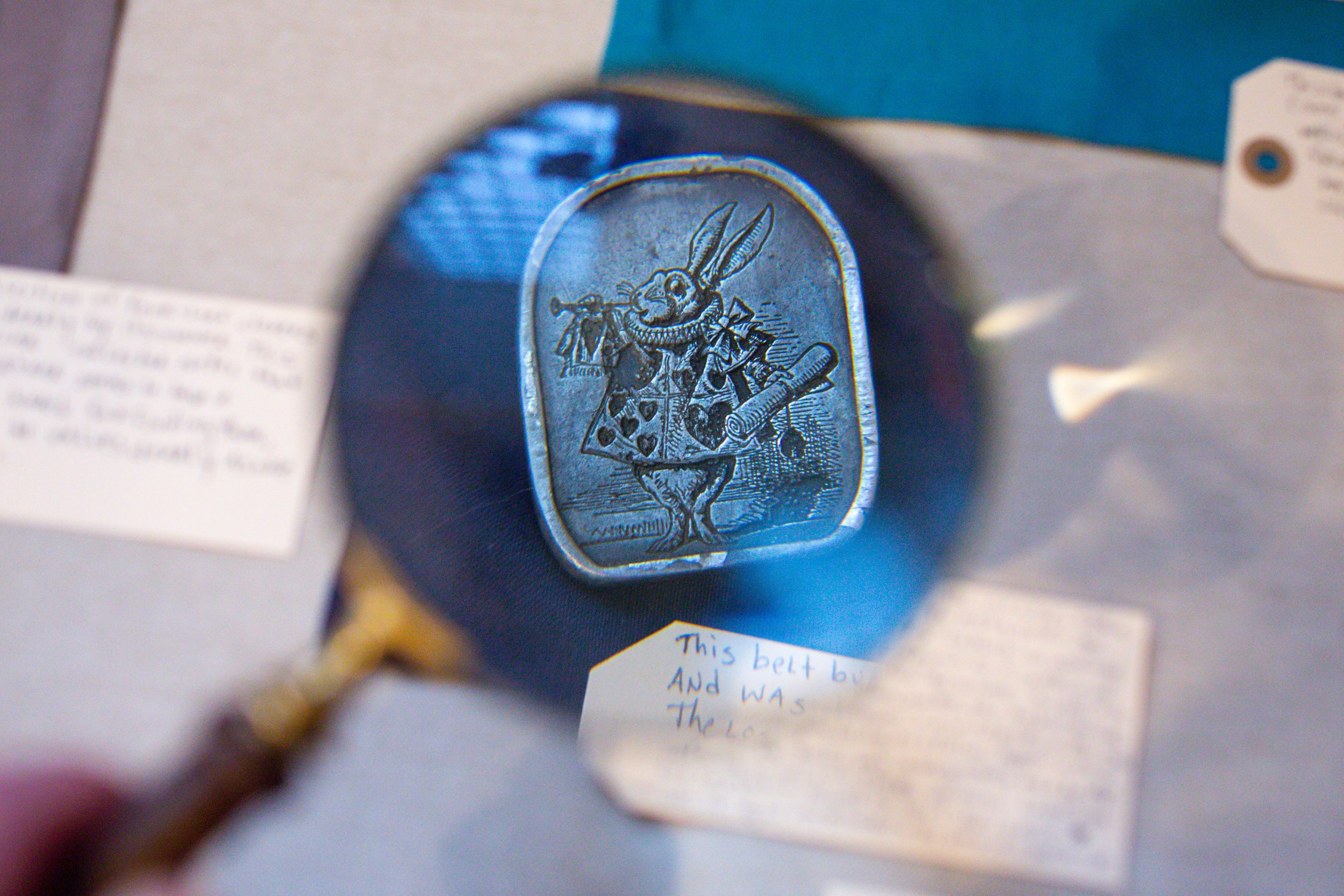 Close-up of a silver brooch featuring the White Rabbit from Alice in Wonderland, holding a trumpet, with a scroll in its hand.