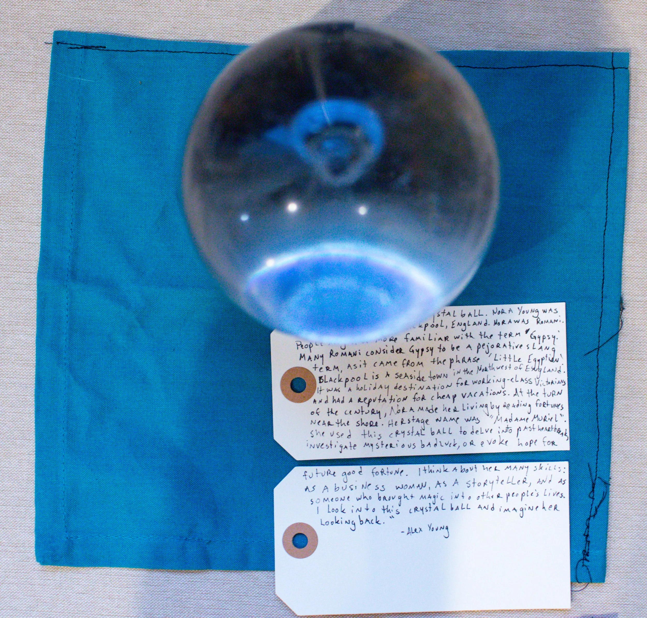 A clear crystal ball is placed on a blue napkin, with a handwritten note underneath.
