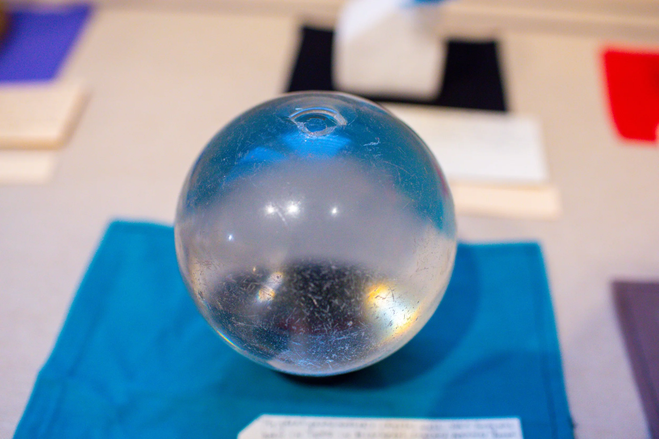 A transparent glass sphere placed on a blue cloth, with blurred books and objects in the background.