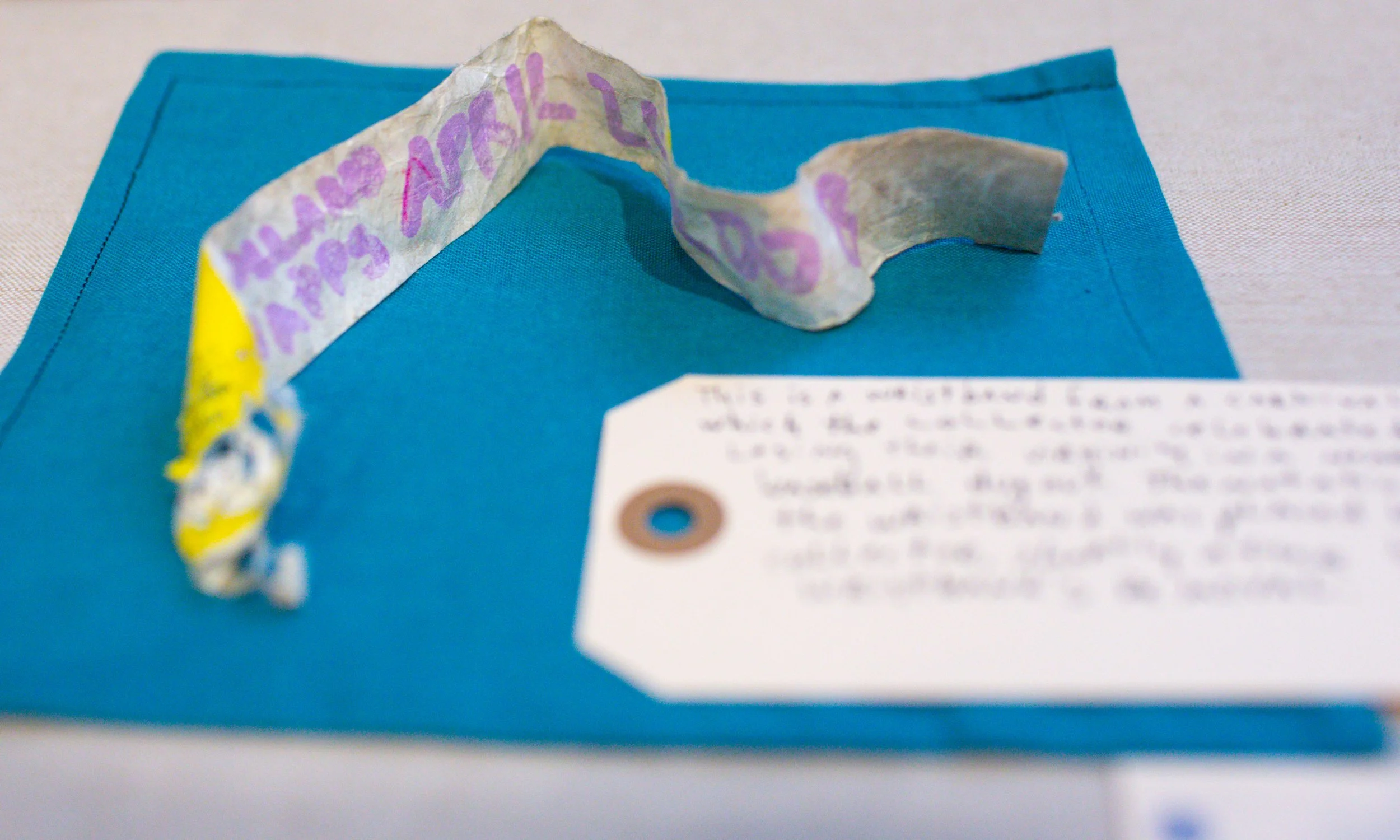 A crumpled piece of paper with handwritten text in purple ink, placed on a blue folder or workspace with a blurred handwritten note in front.