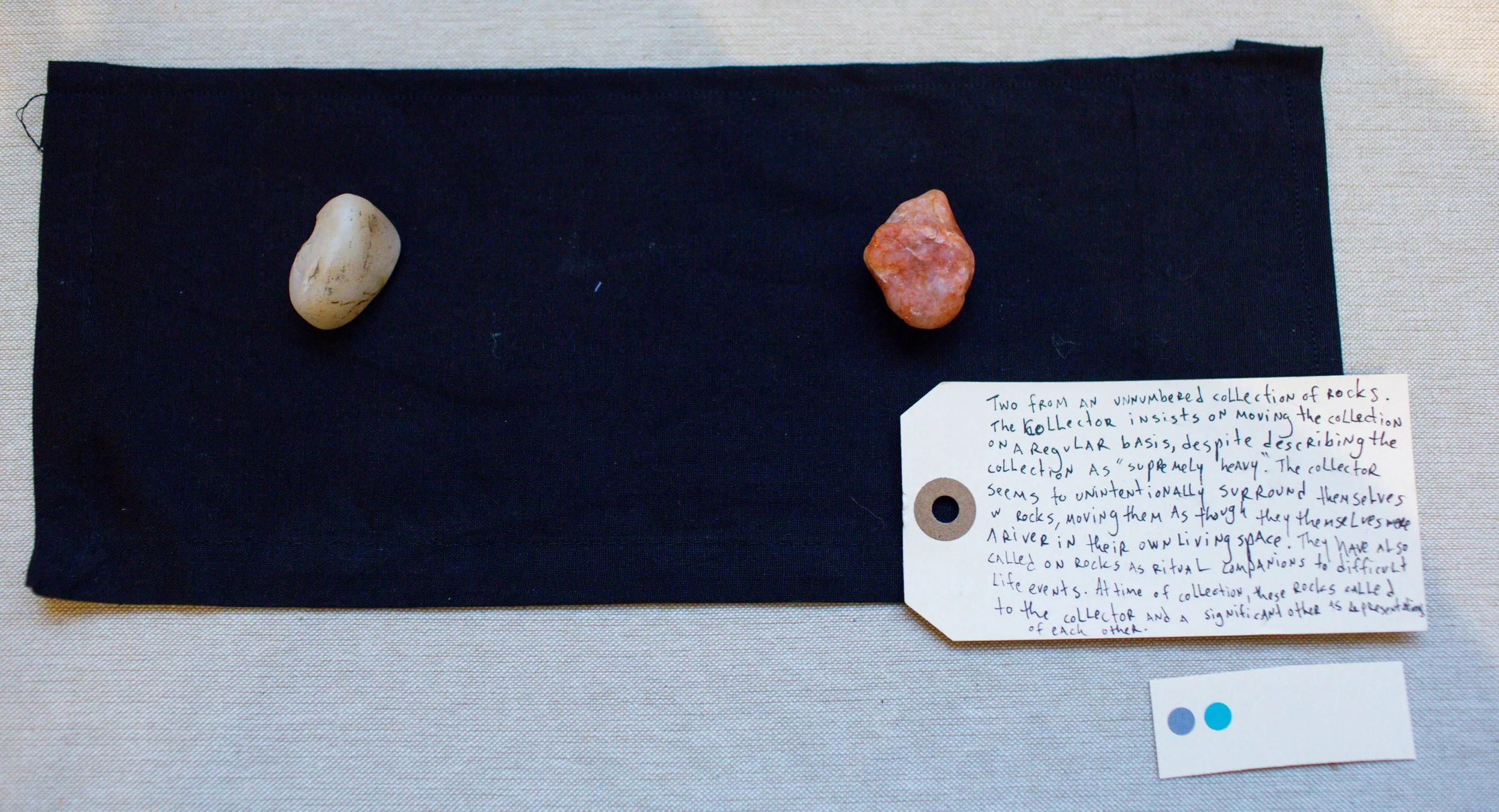 Two rocks from an unnumbered collection are displayed on a black cloth. A handwritten note explains the rocks' significance as ritual companions and their role in the collection, which is maintained by a collector.