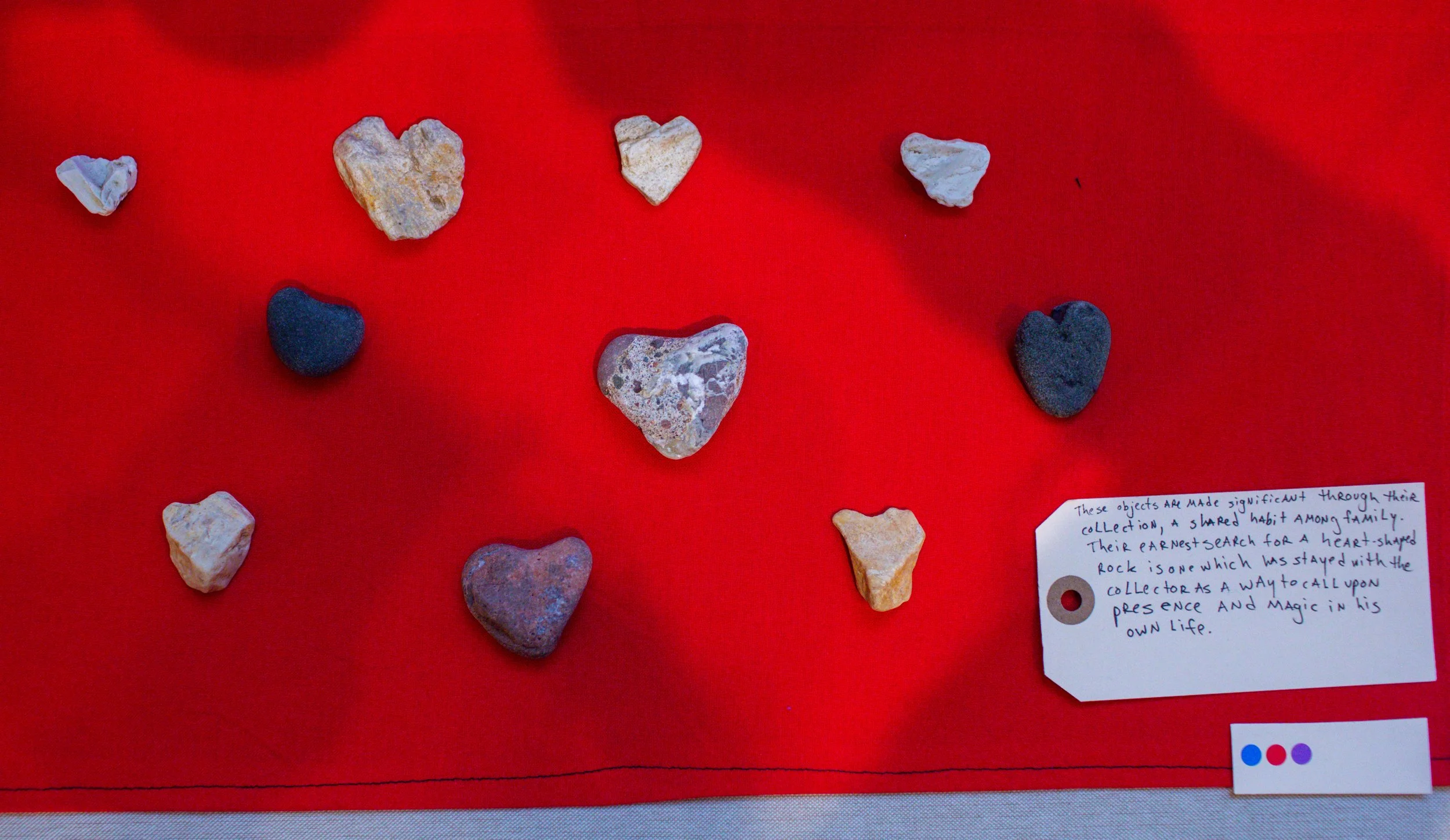 Various heart-shaped stones and rocks on a red surface, with a handwritten note and a color selection tag.