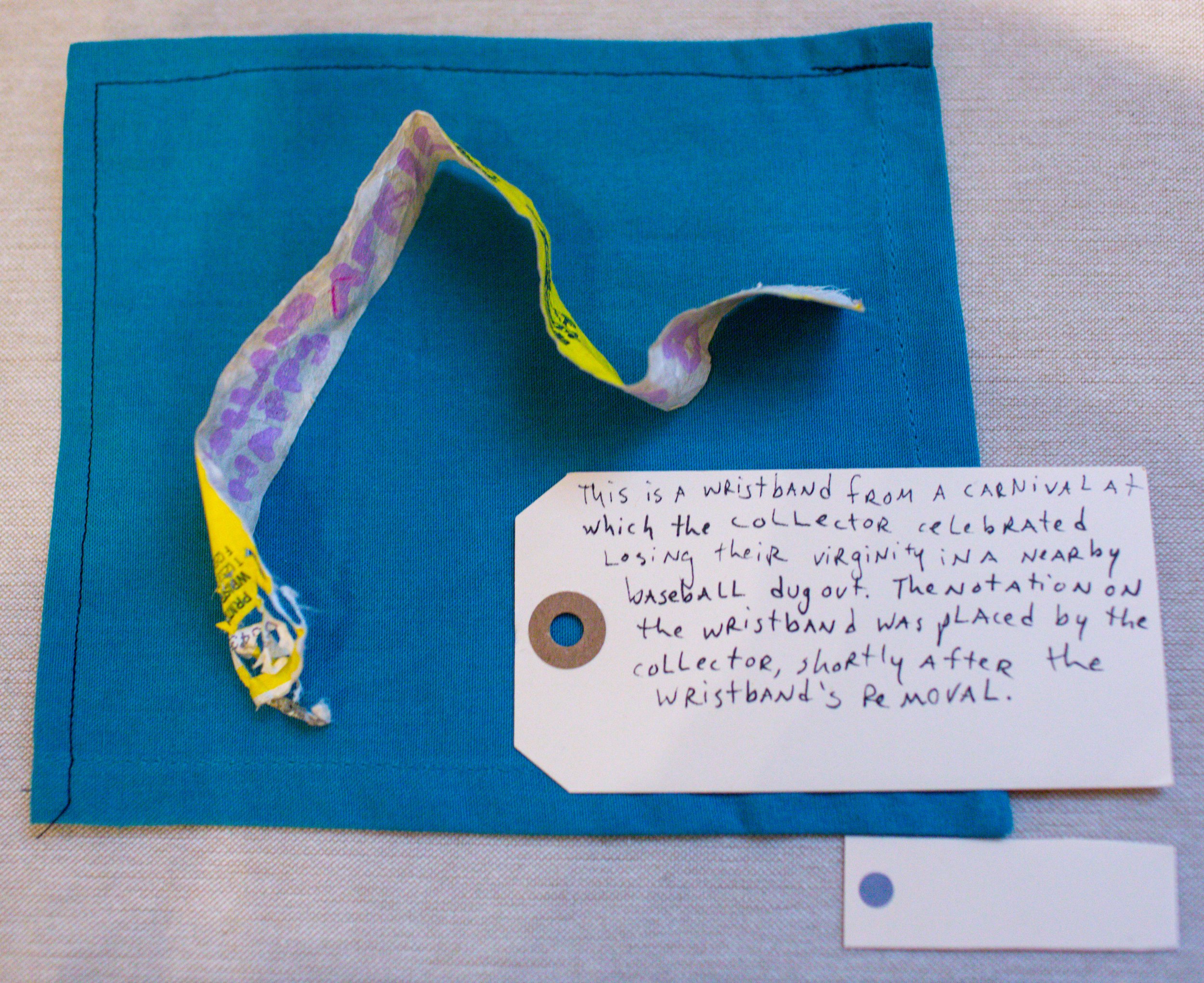 A worn wristband from a carnival placed on a blue fabric surface with a handwritten note explaining its significance.