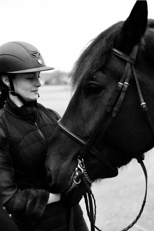 A woman in riding gear and a helmet gently touching noses with a dark horse.