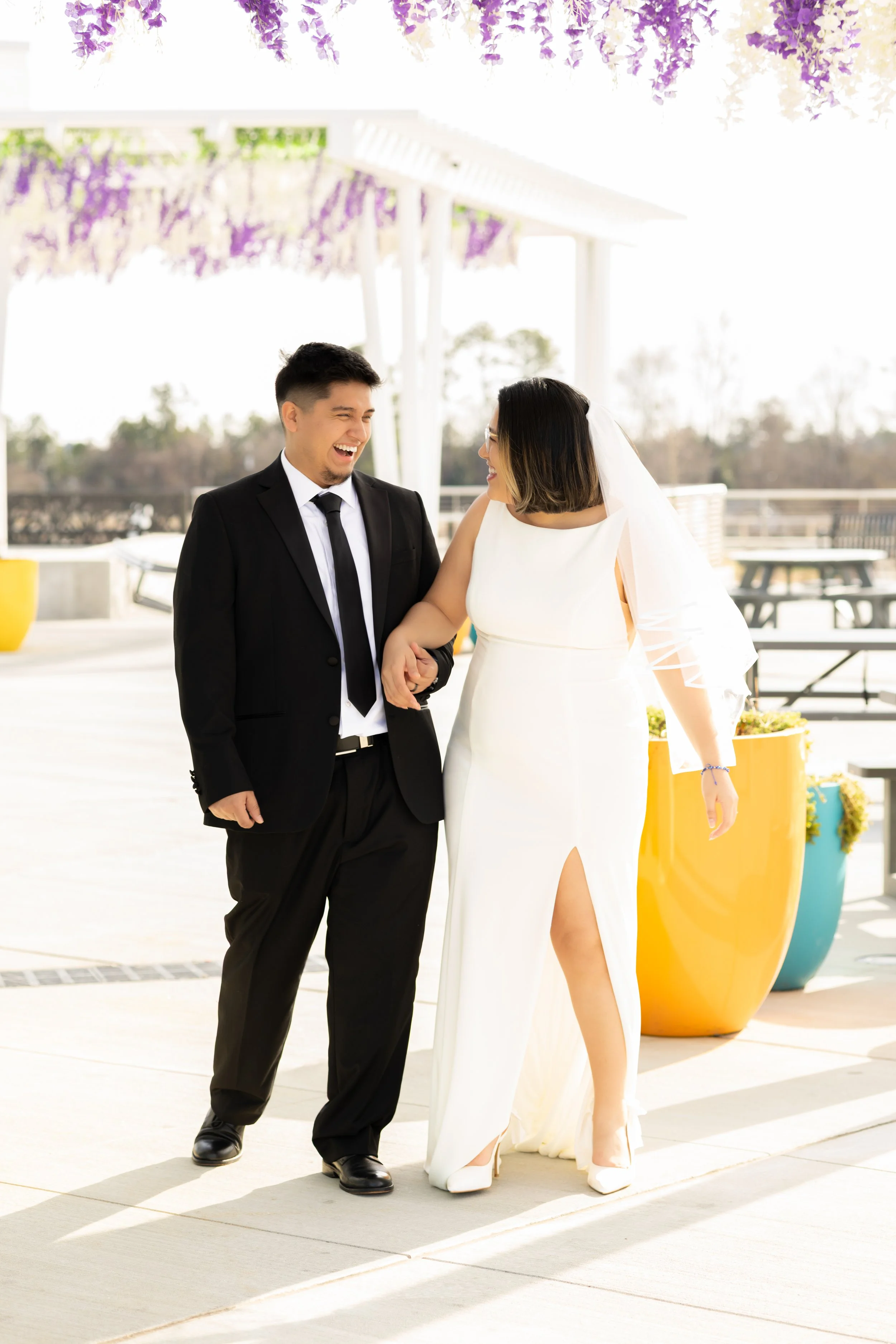 Happy bride and groom walking arm in arm outdoors on their wedding day, smiling at each other in Suwanee, GA following a micro wedding.