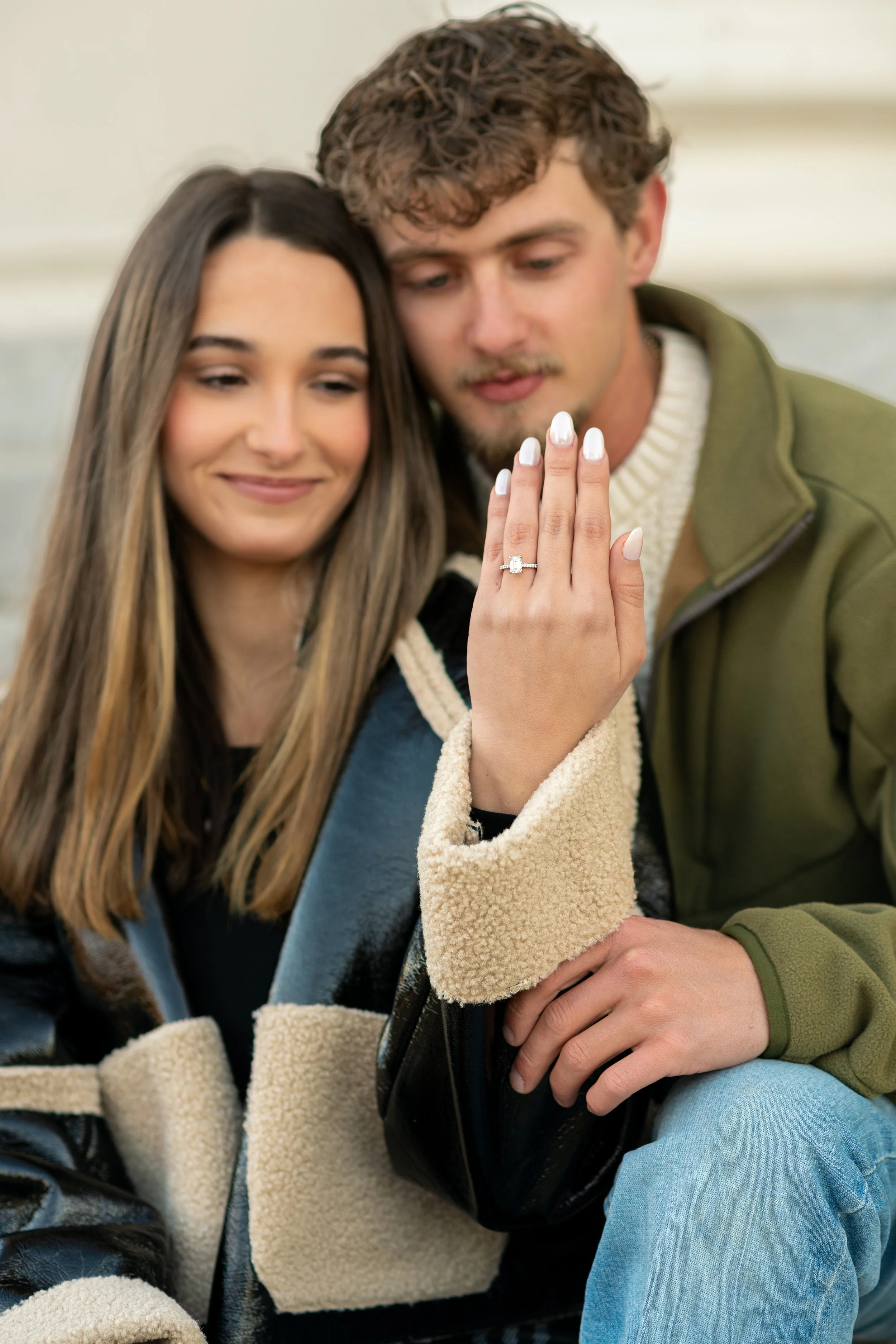 A happy couple showing off an engagement ring, with the woman displaying her hand and ring.