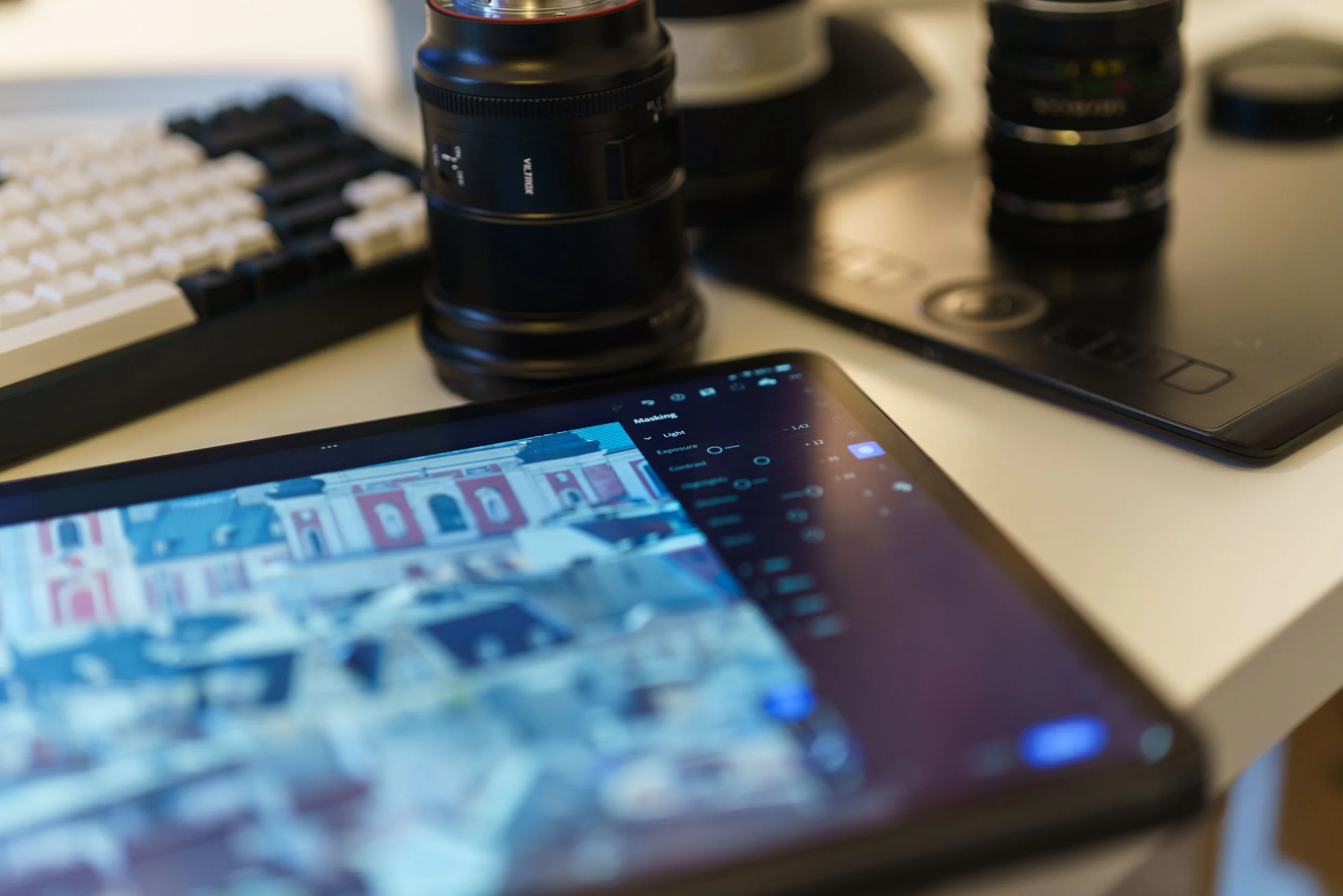 A modern workspace featuring a tablet, camera lenses, and graphic drawing tablet on a desk.