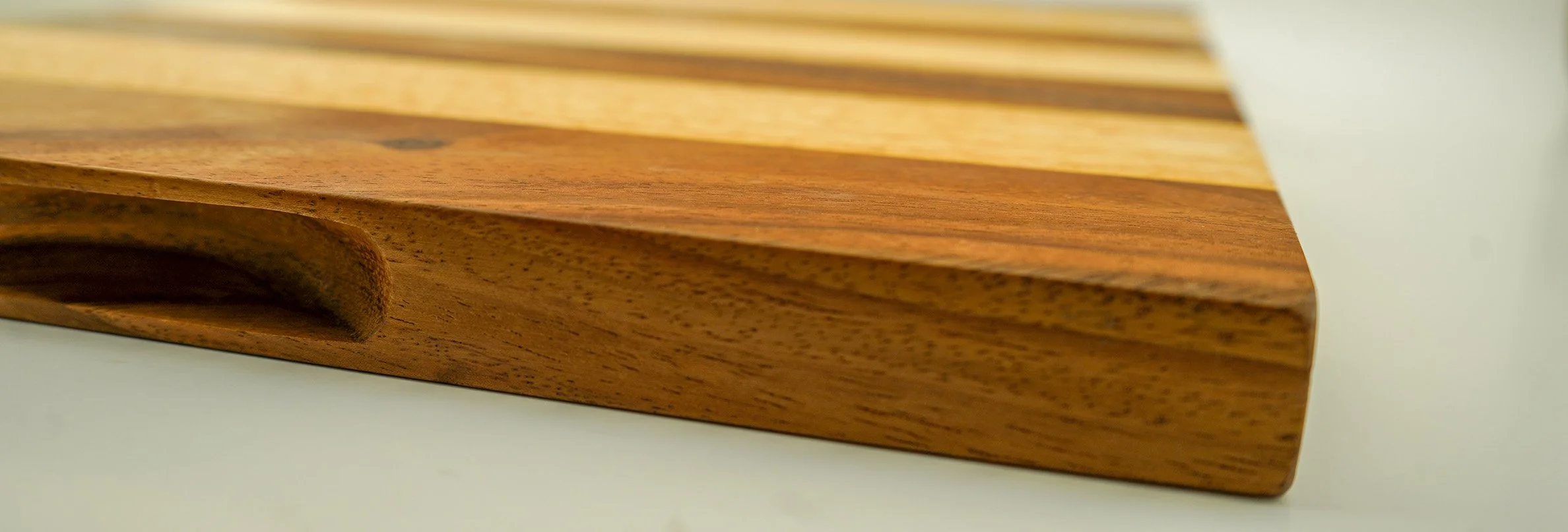 Close-up of a wooden cutting board with a smooth, curved groove on the edge, placed on a white surface.