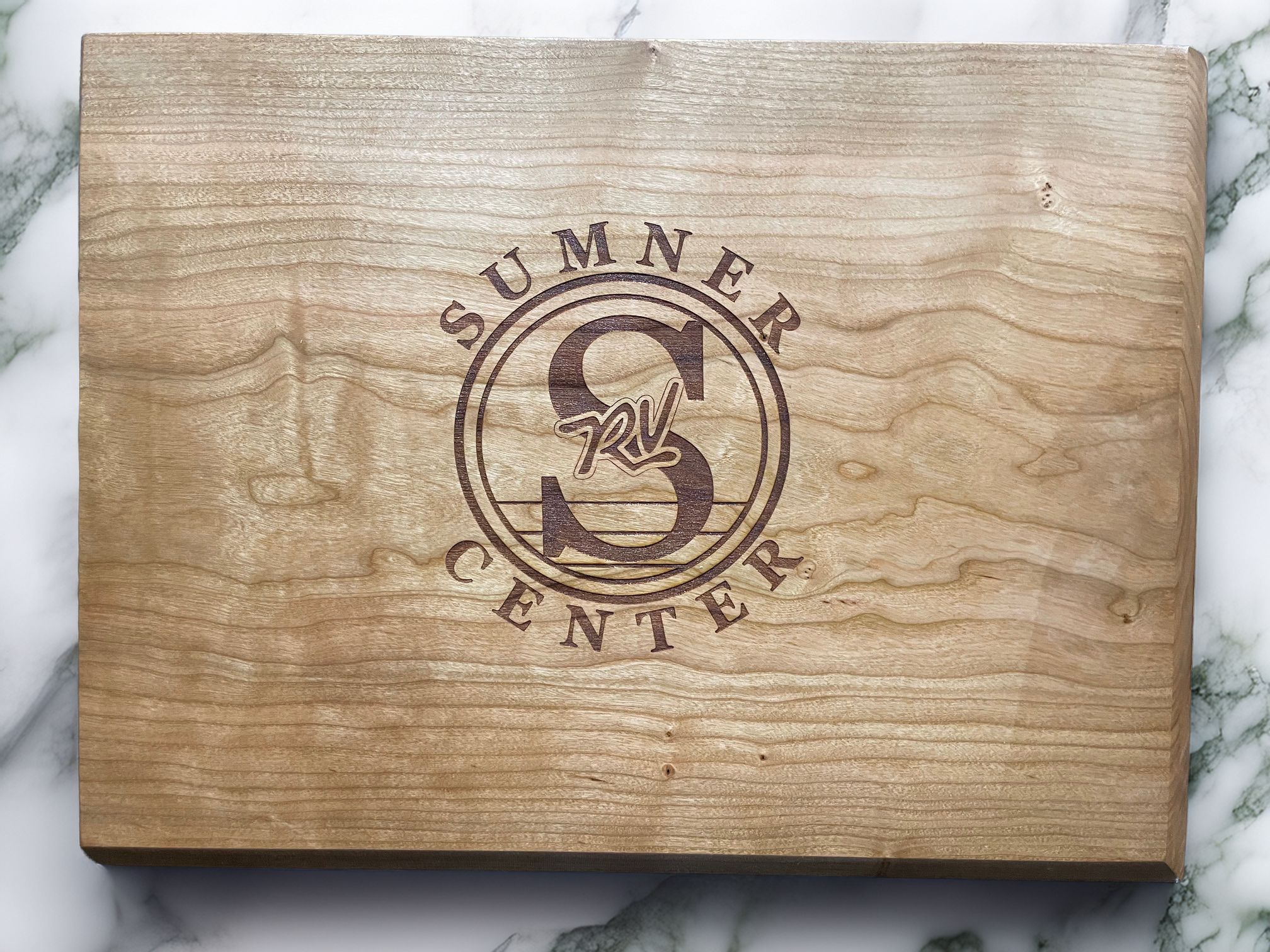 A wooden box with a circular logo engraved on the lid that reads "Summner Center" and features a large number 3 with the letters RL crossing the middle.